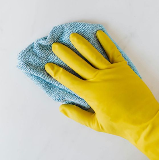 Someones hand wearing yellow rubber gloves and using a blue rag to clean a white surface