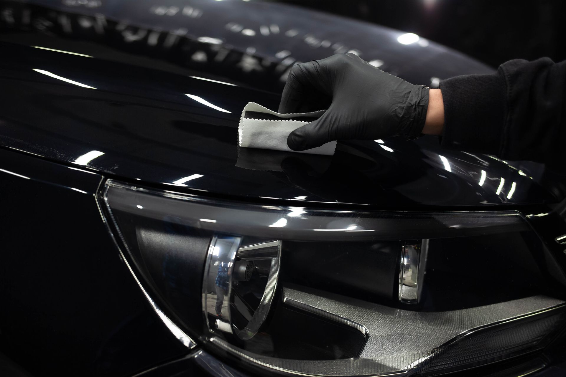A person wearing black gloves is polishing the hood of a black car.