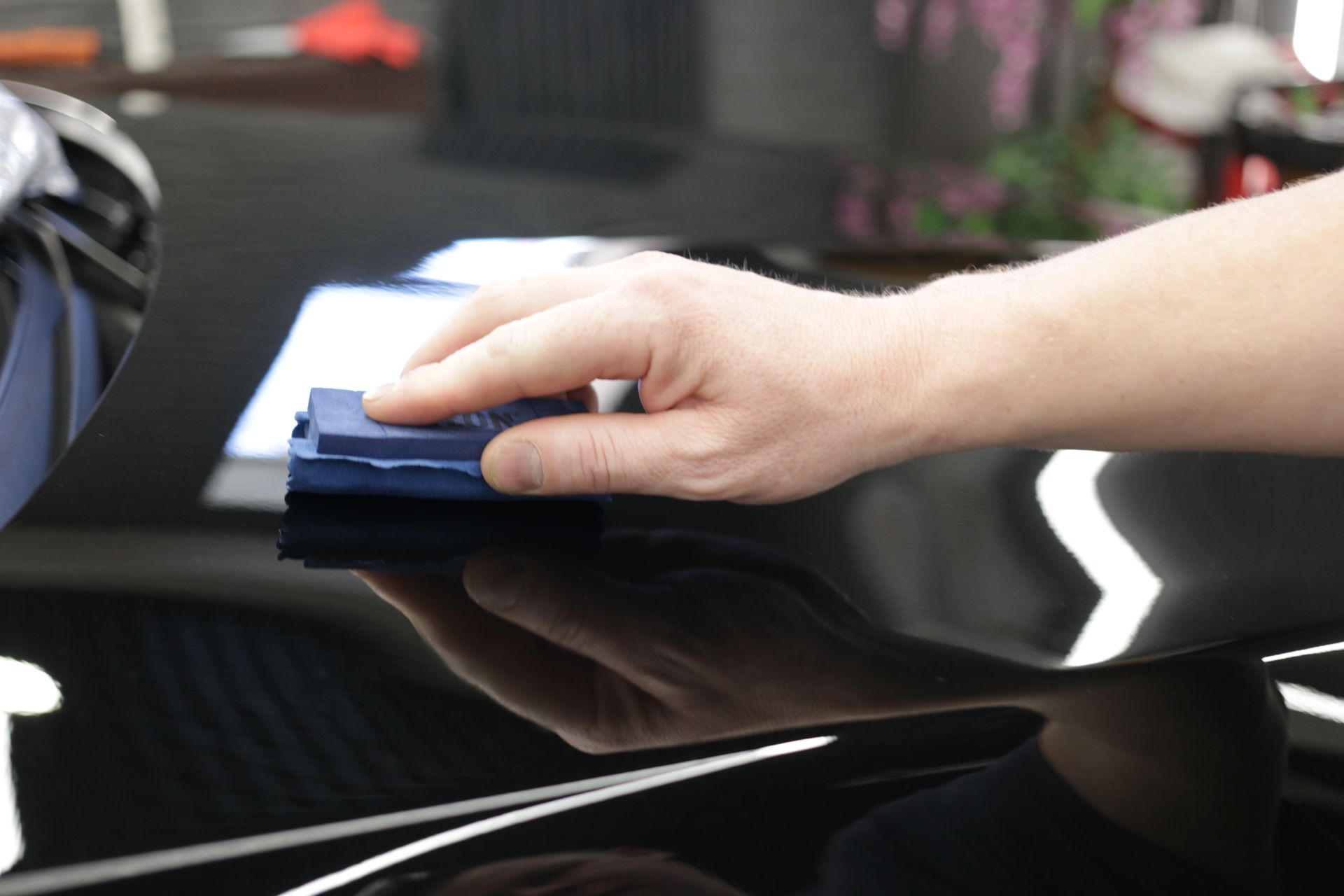 A person is polishing the hood of a black car.