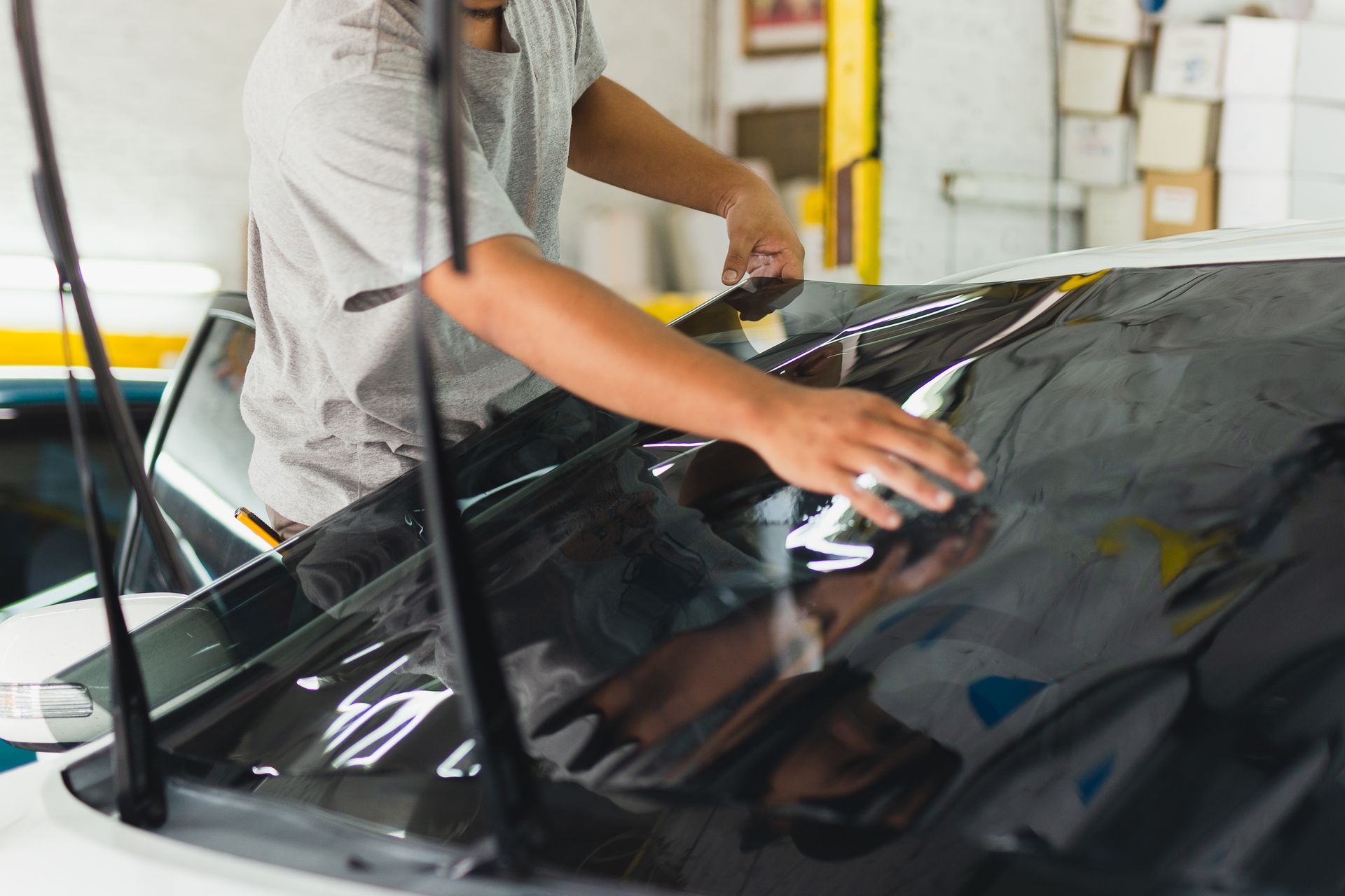 A man is applying tinted glass to the windshield of a car.