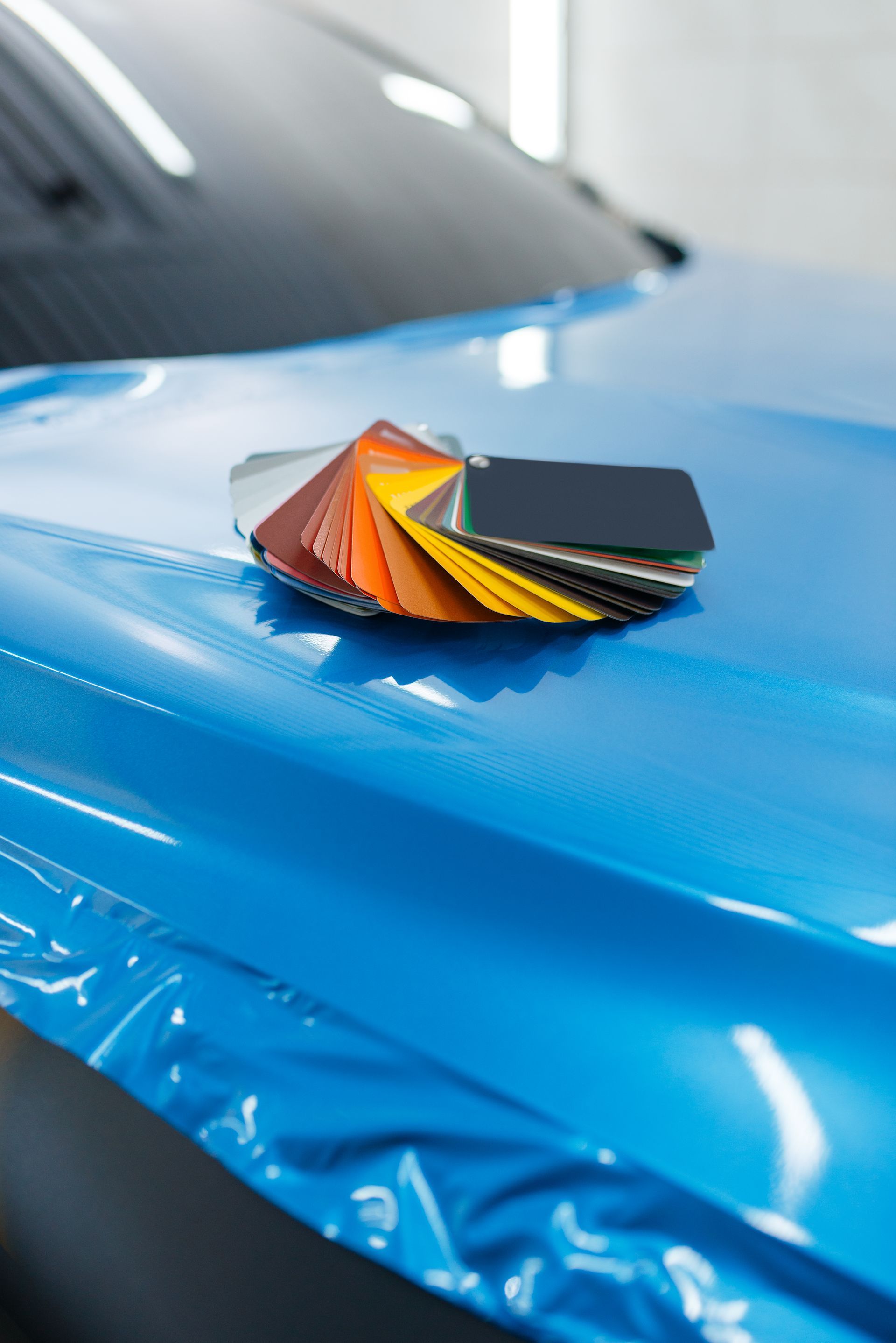A blue car is being wrapped in plastic and there are samples of different colors on the hood.
