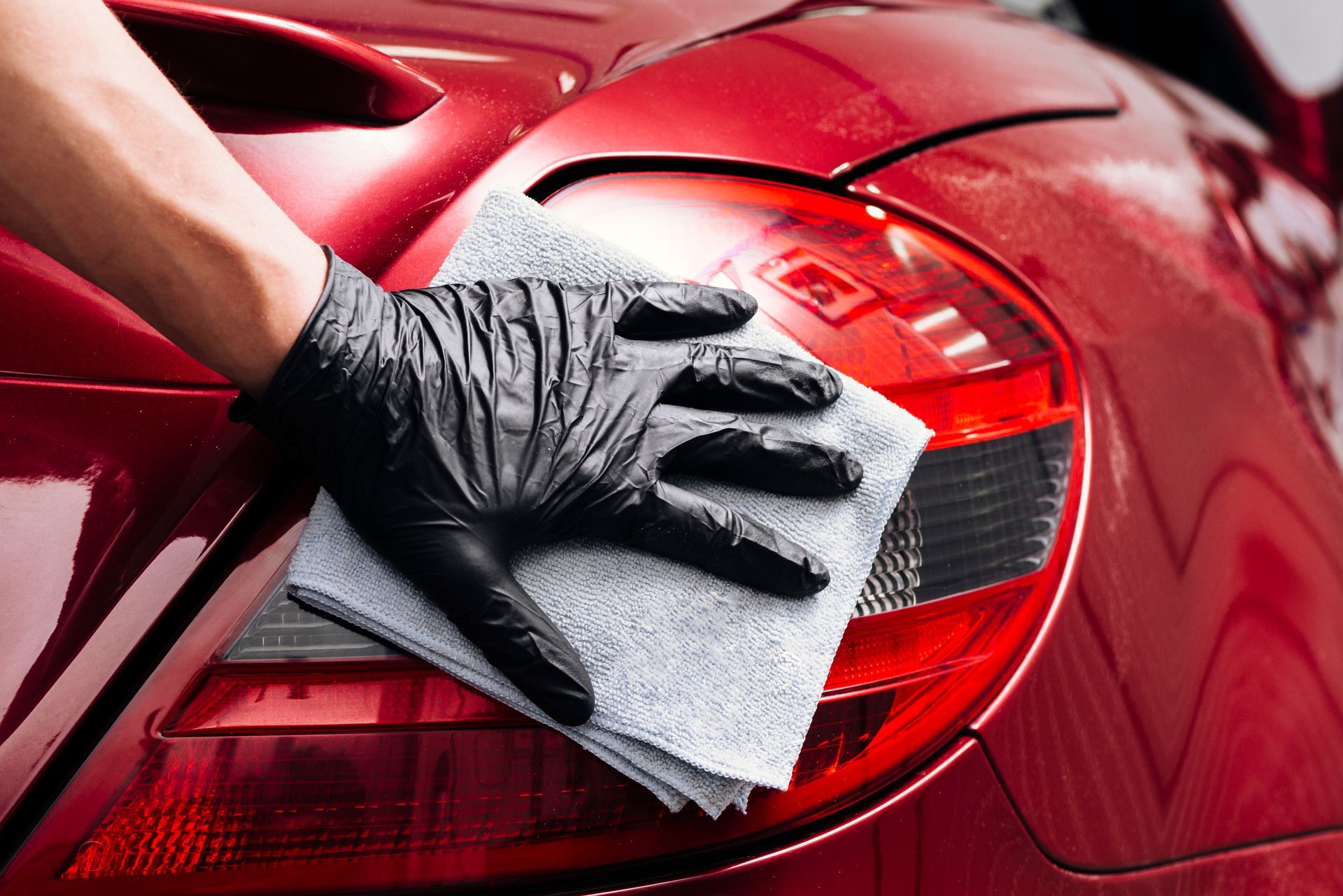 A person wearing black gloves is cleaning a red car with a towel.