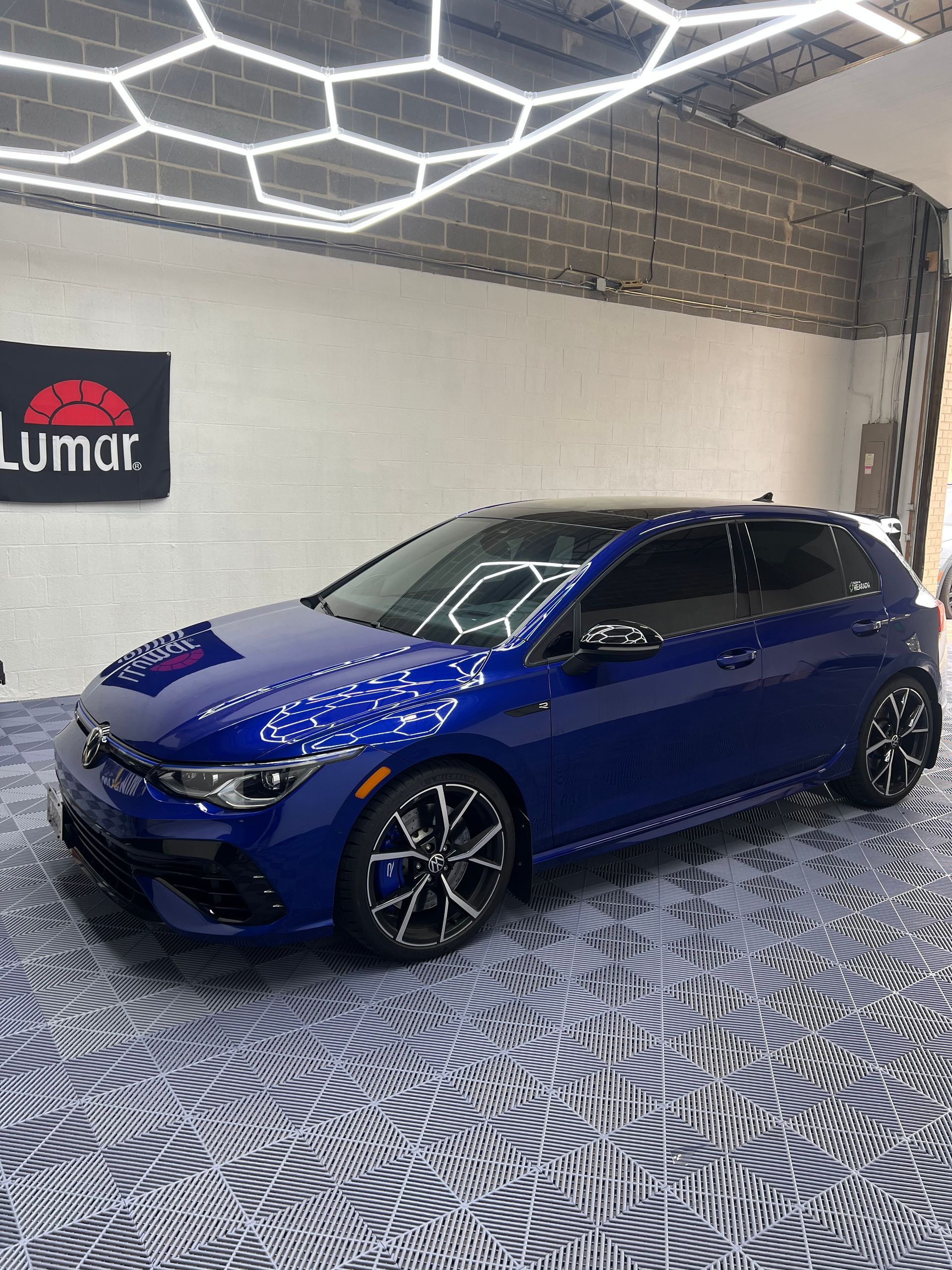 A blue car is parked in a garage next to a lumar sign.