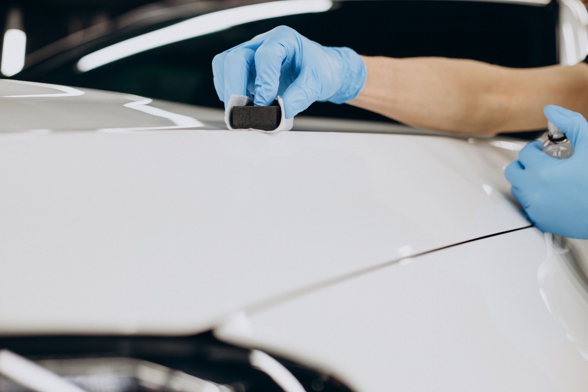 A person wearing blue gloves is polishing the hood of a white car.