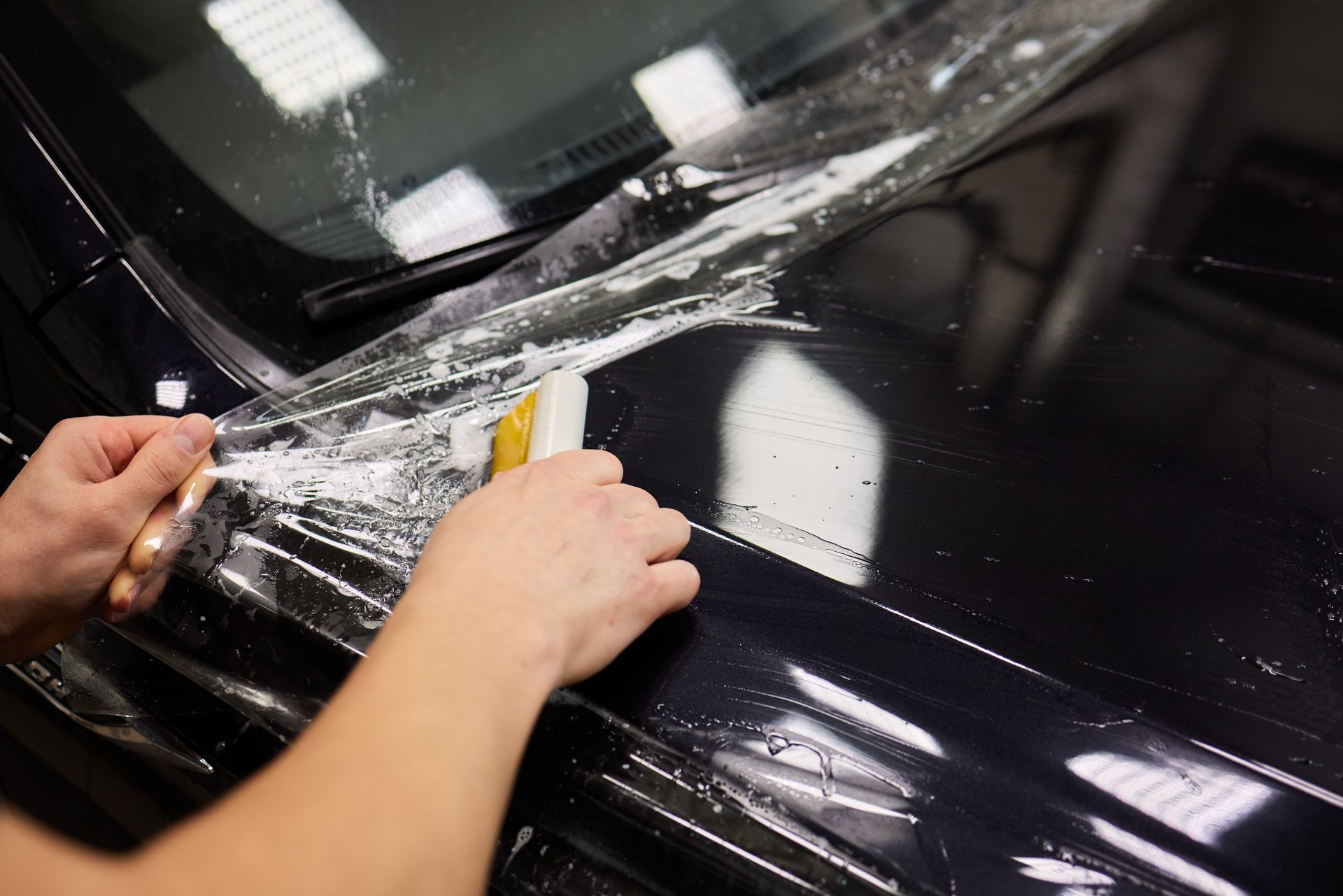A person is applying a protective film to the hood of a car.