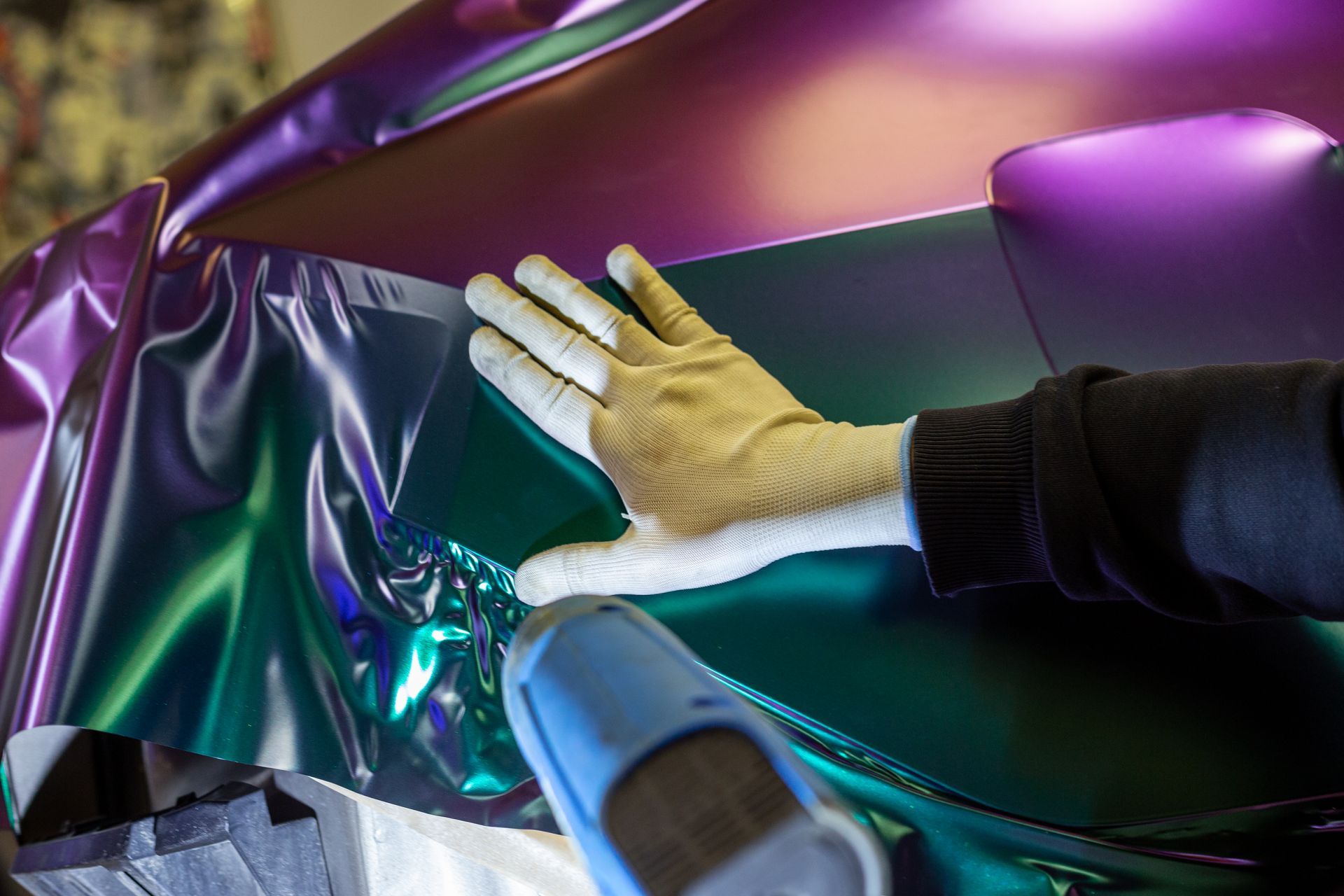 A person is wrapping a car in purple and green foil.