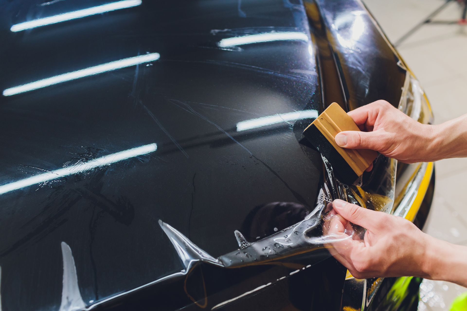 A person is applying a protective film to the hood of a car.