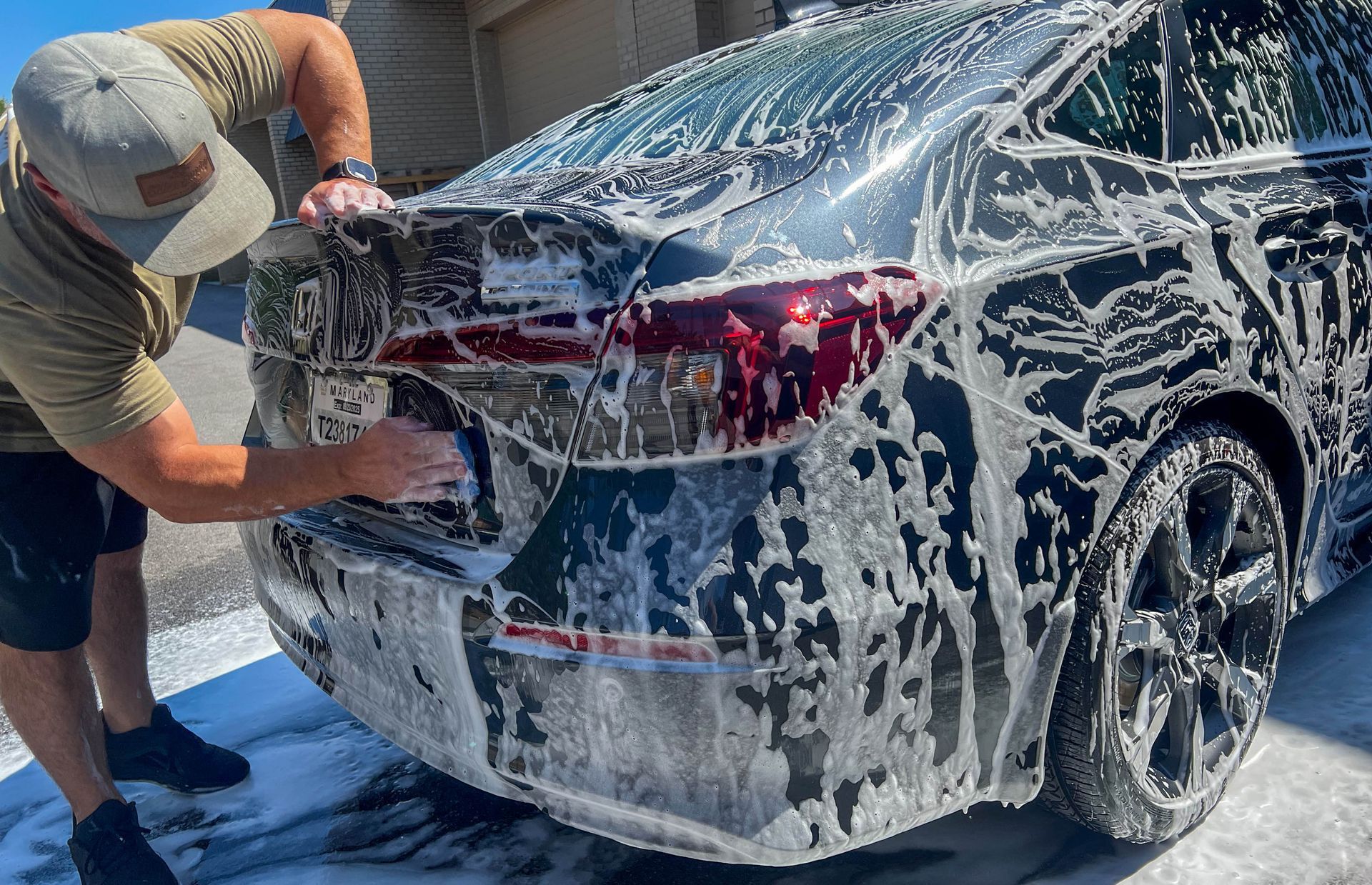 Man washing a black car, covered in white soap suds, outside.