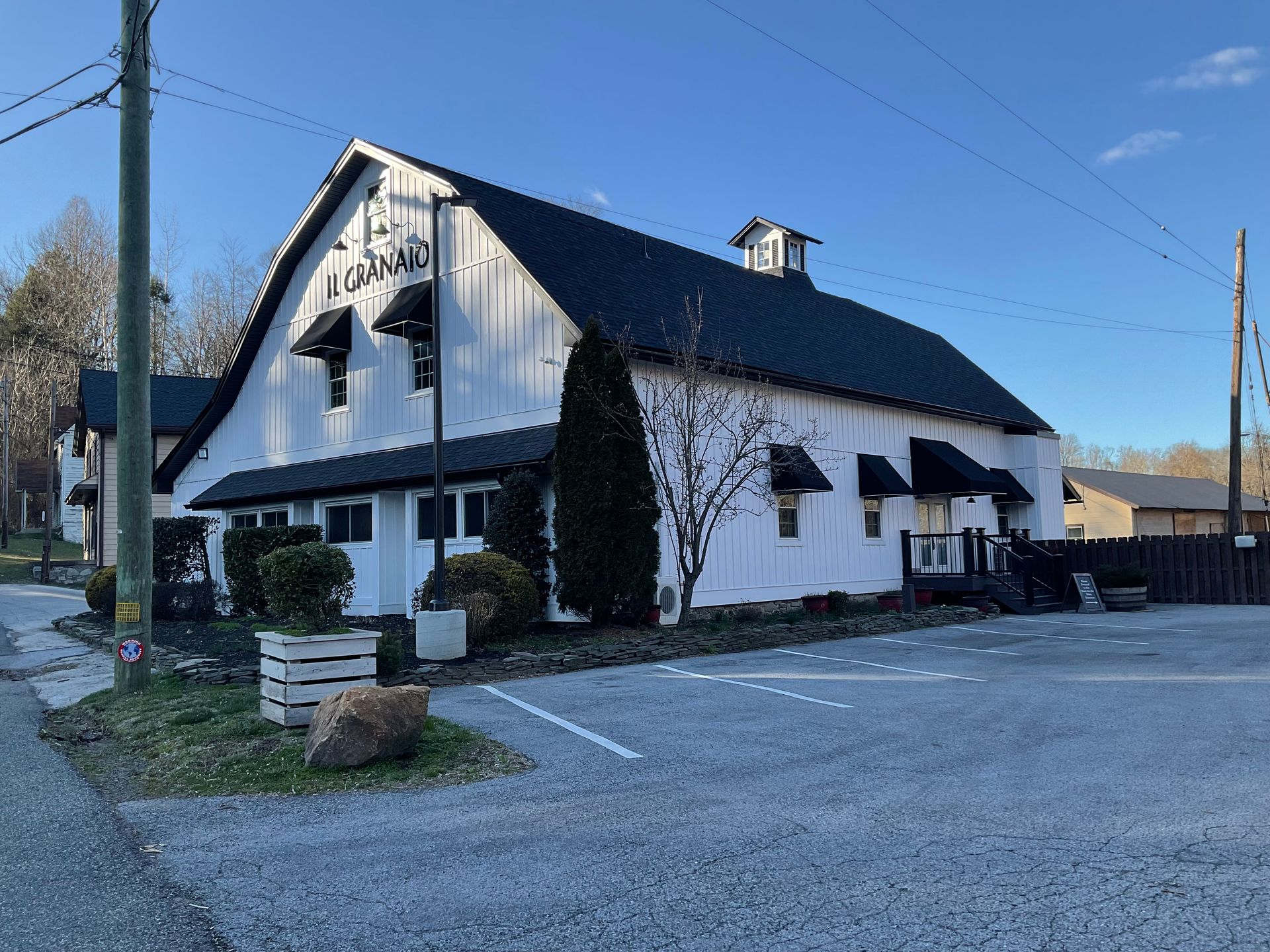A white barn with a black roof and a parking lot in front of it.