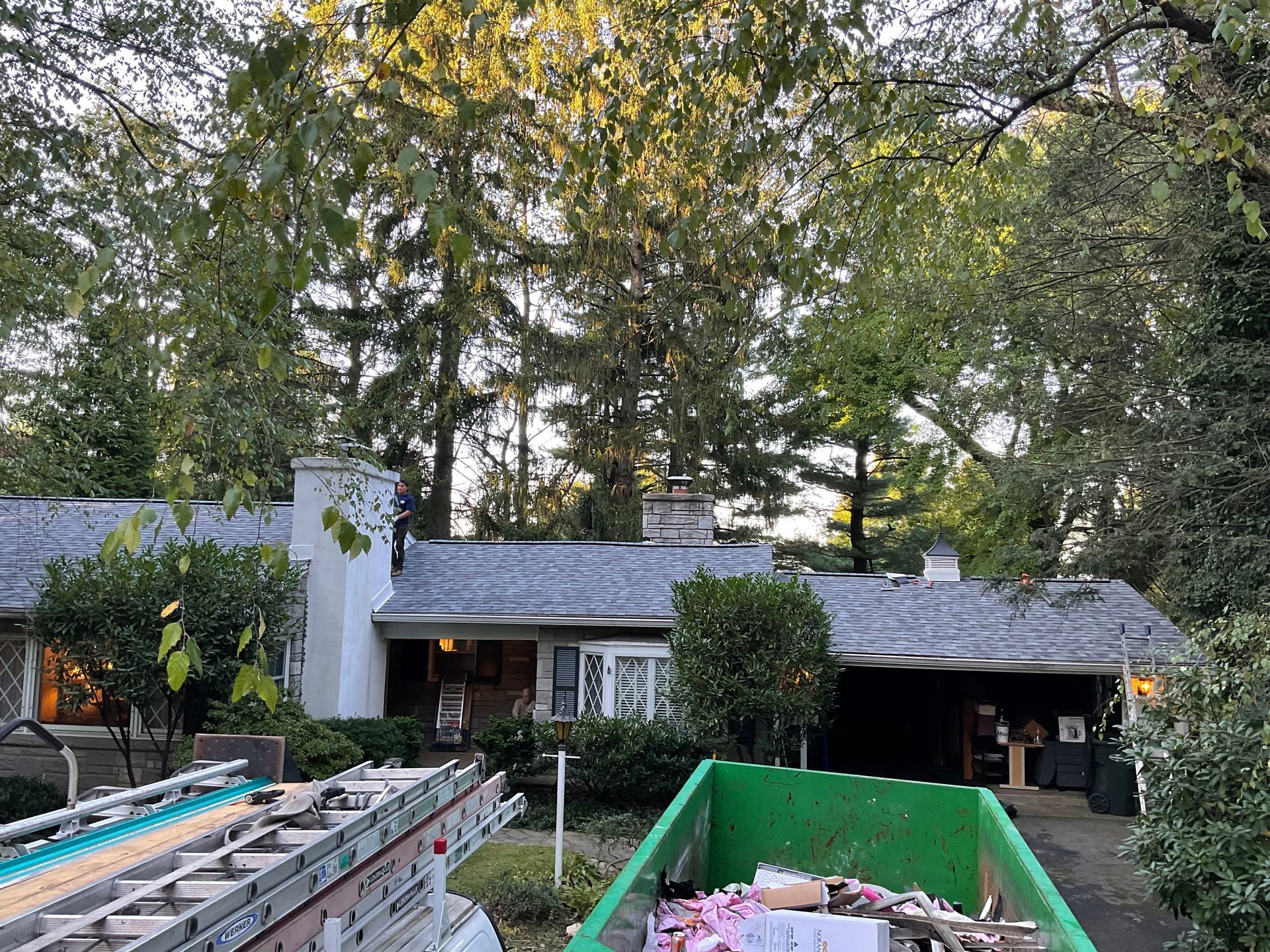 A green dumpster is sitting in front of a house.