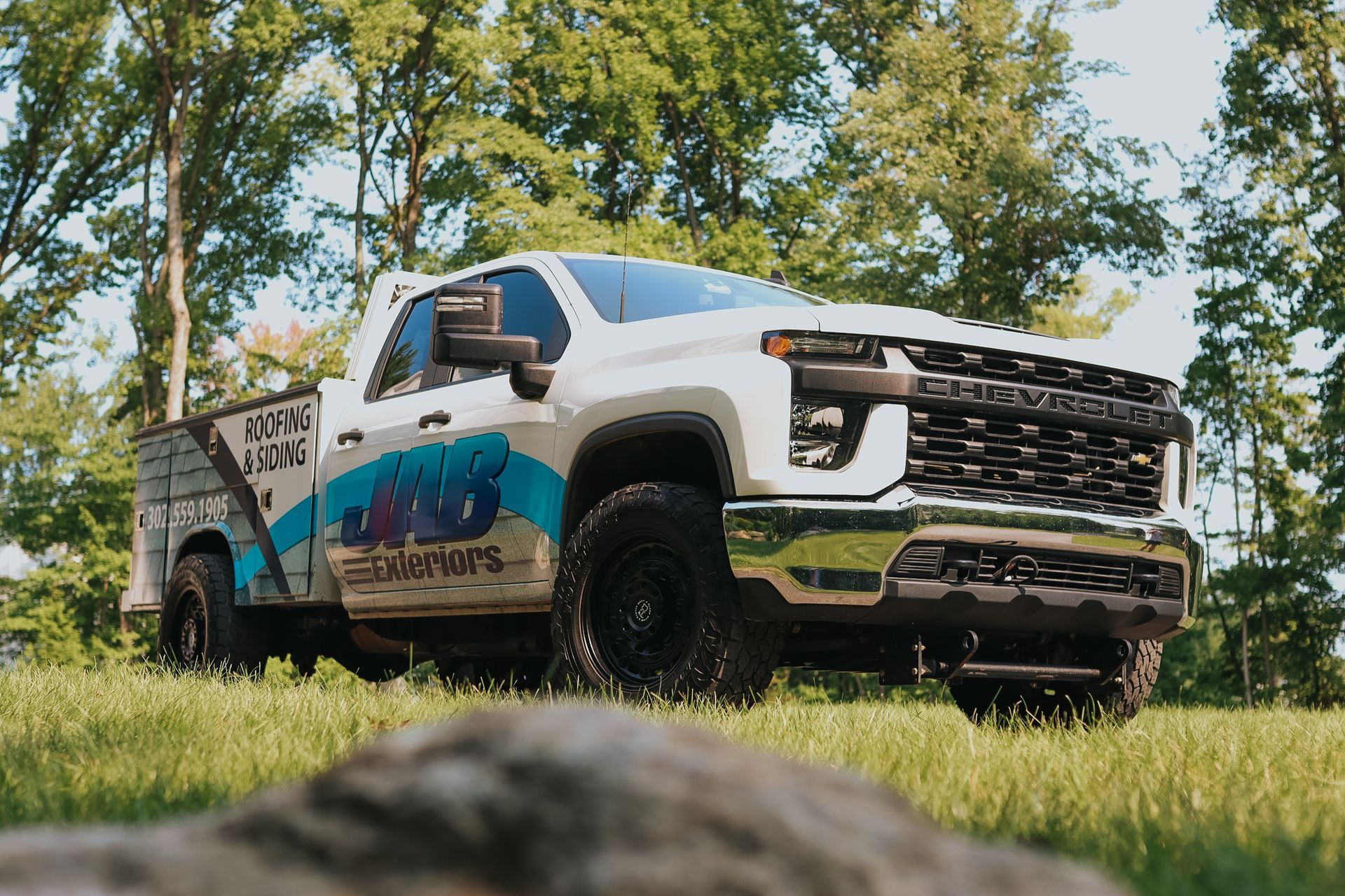 A white roofing company truck is parked in a grassy field.