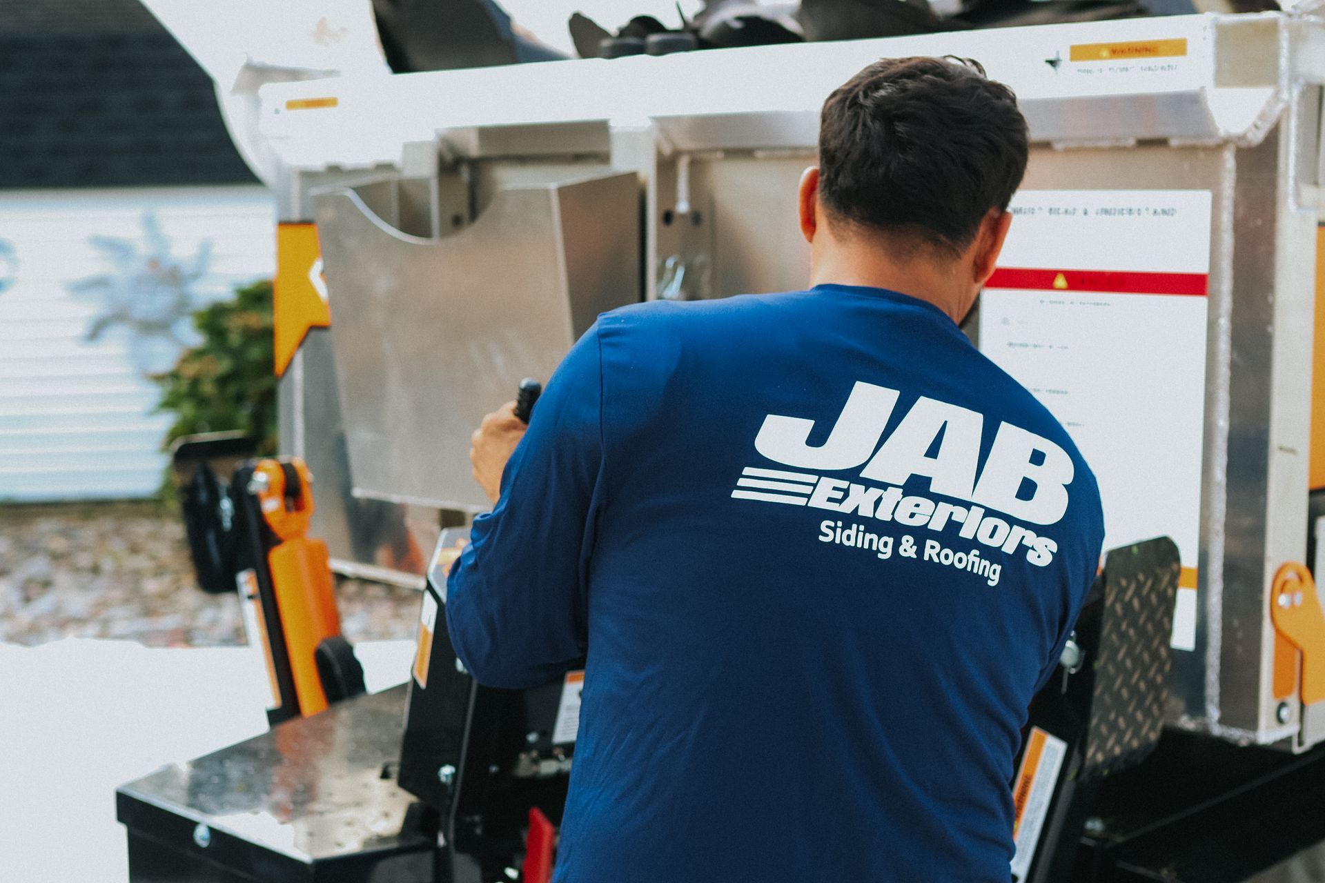 A man wearing a blue shirt that says jab exteriors is loading a dumpster.