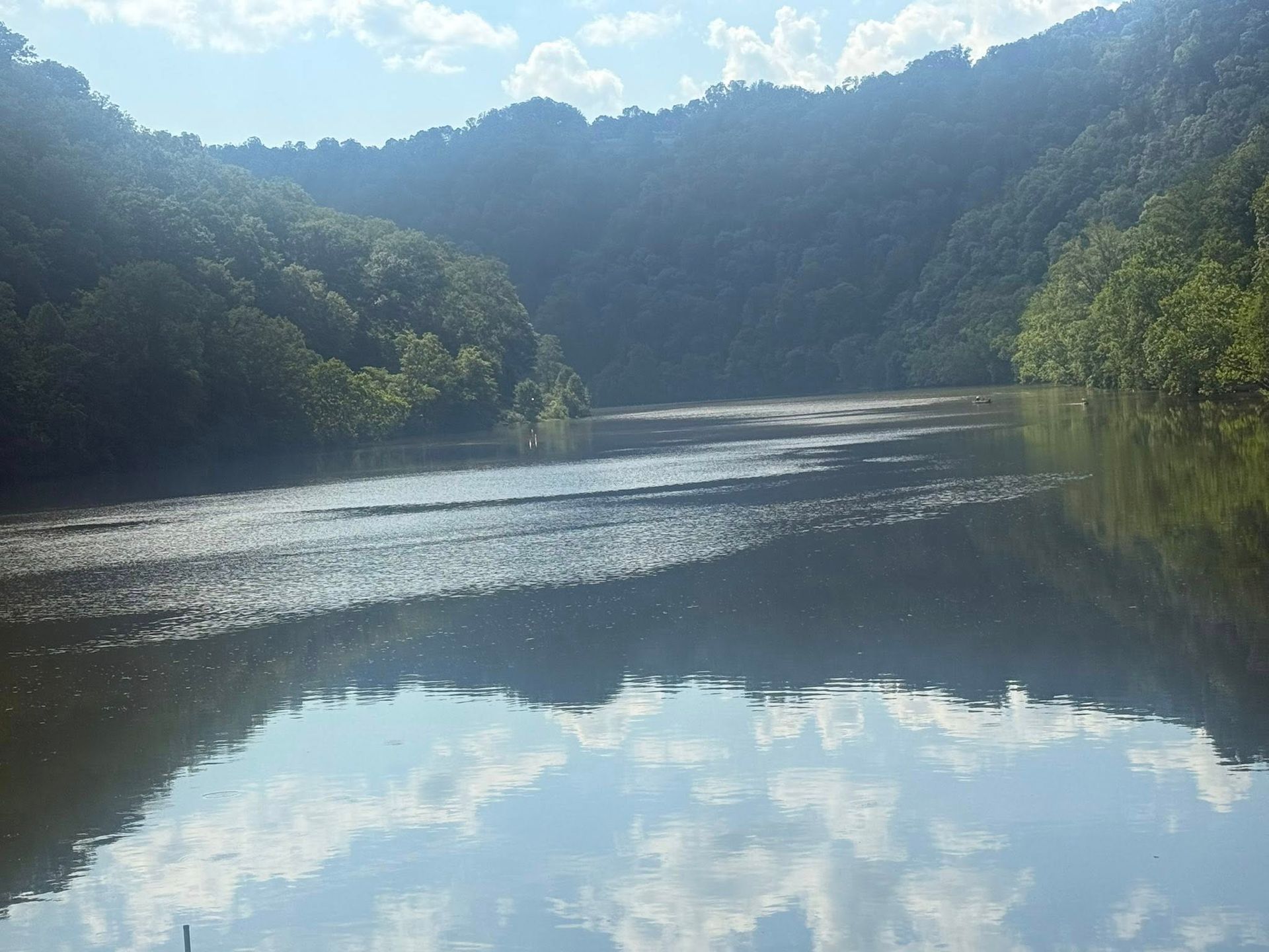 A calm river reflects the sky and surrounding green trees, with a mountainous backdrop.