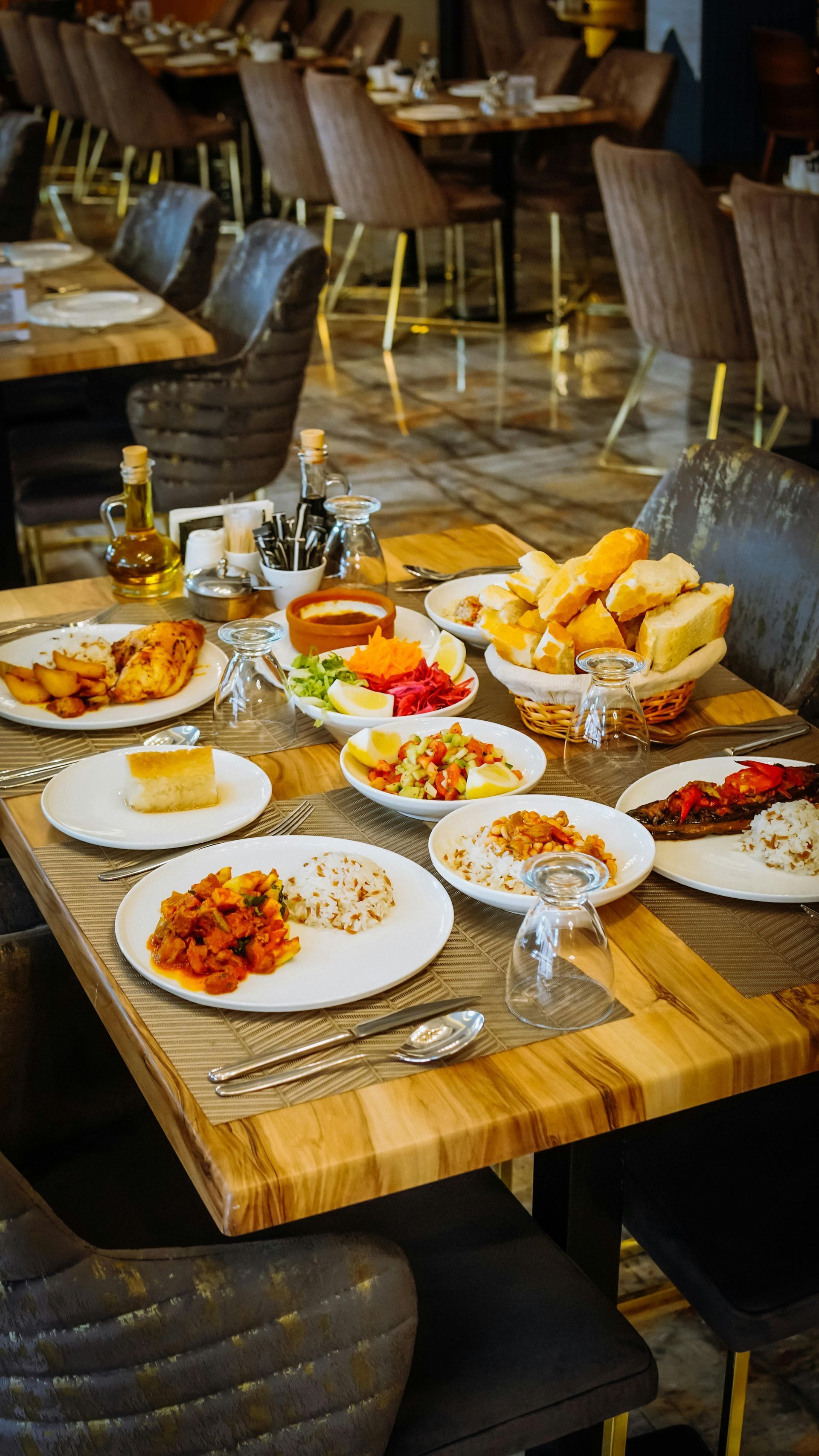 Table set with assorted dishes and bread in a restaurant, with brown tables and chairs.