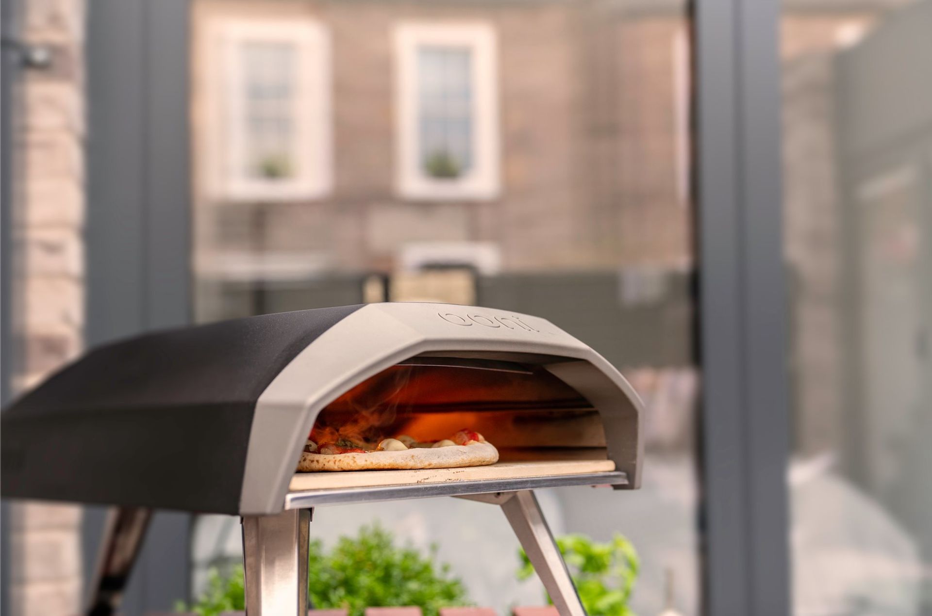 Um forno de pizza está do lado de fora de um prédio, próximo a uma janela.