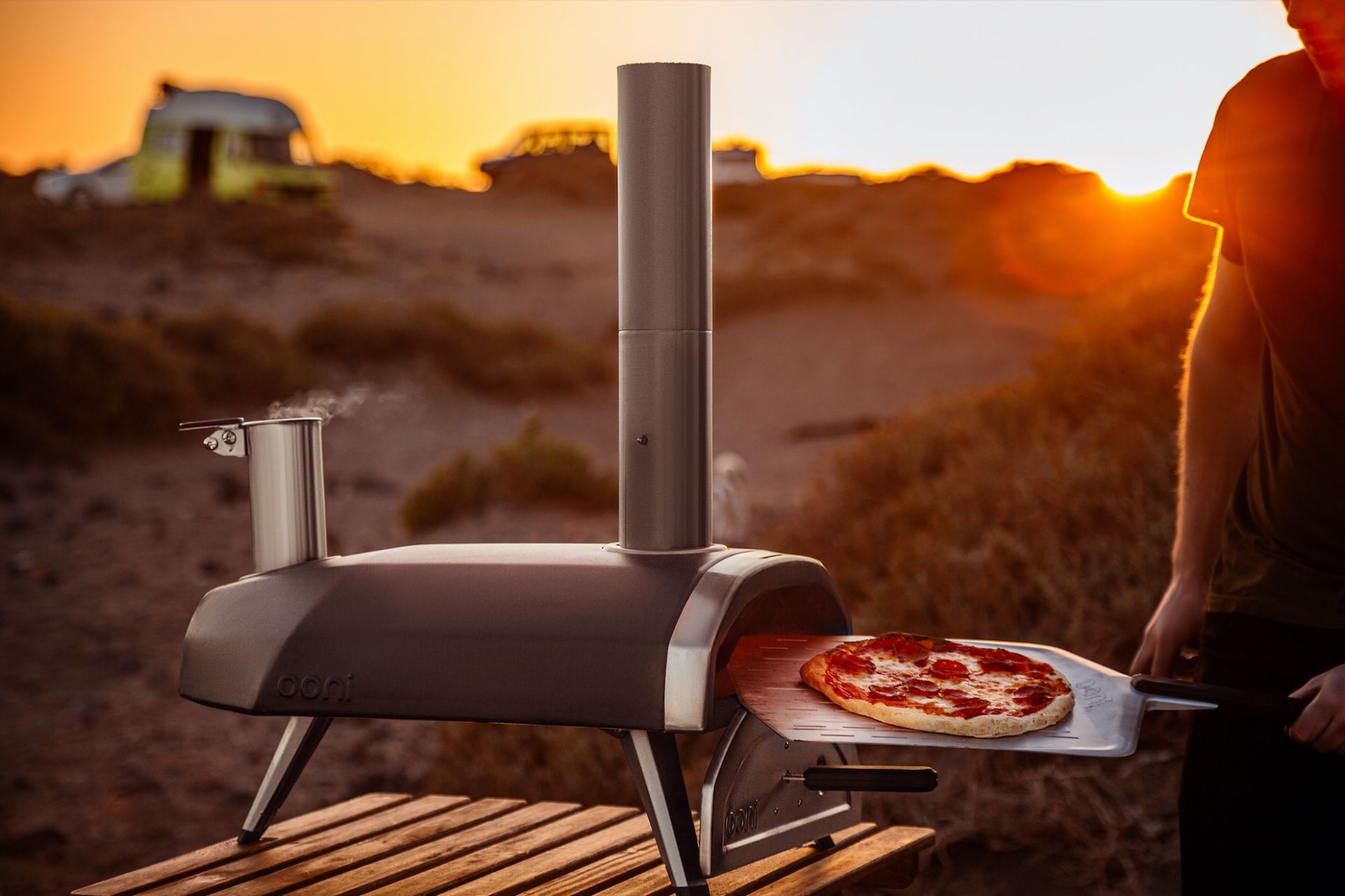 Um homem está segurando uma pizza na frente de um forno de pizza.