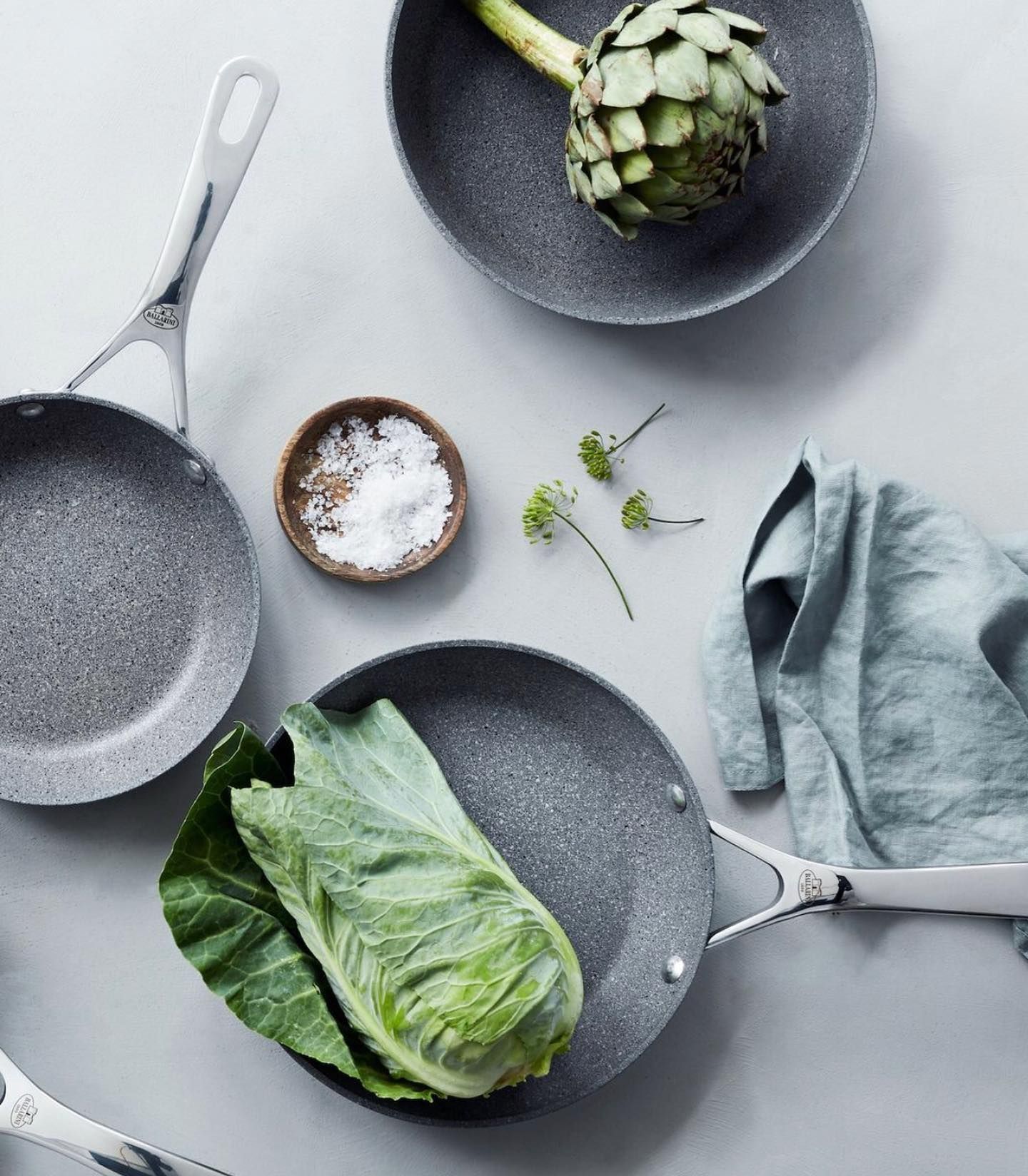 Uma mesa coberta com panelas, uma tigela de sal, alface e alcachofras.