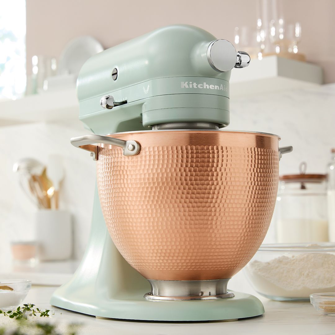 Uma batedeira kitchenaid com uma tigela de cobre está sobre um balcão.