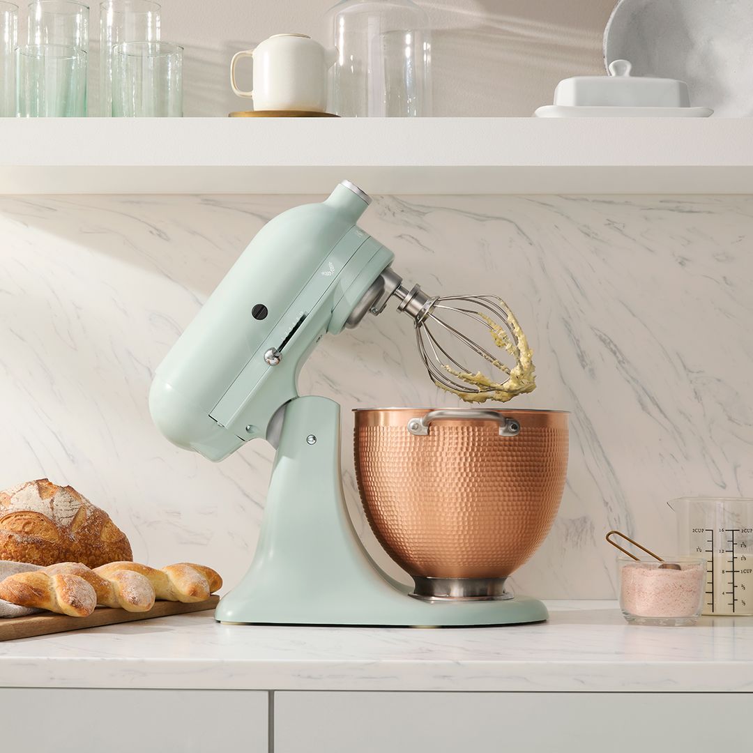 Uma batedeira kitchenaid está em um balcão ao lado de uma tigela de pão.