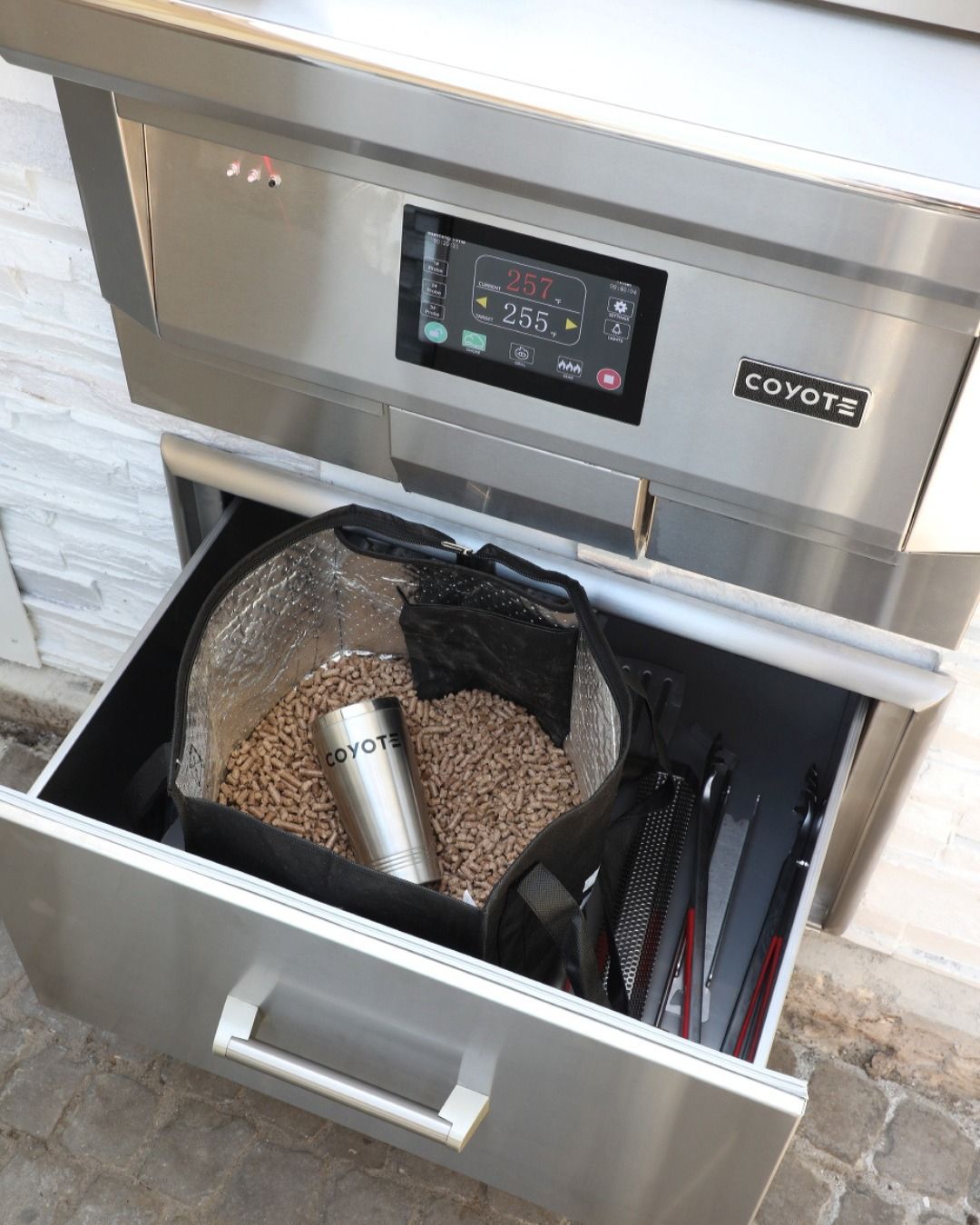 Um forno de inox com gaveta cheia de aparas de madeira.