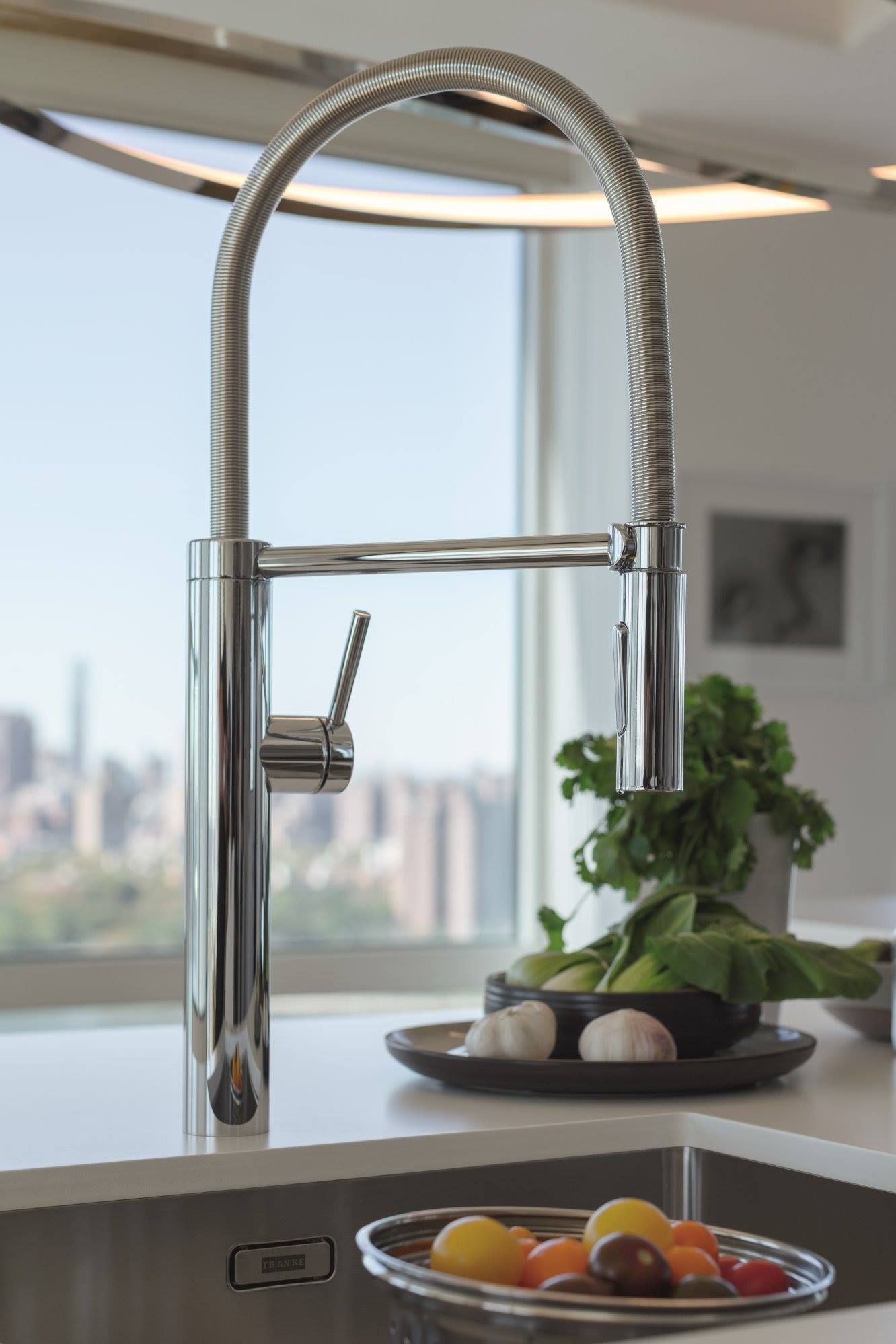 Uma pia de cozinha com torneira e uma tigela de frutas e legumes no balcão.