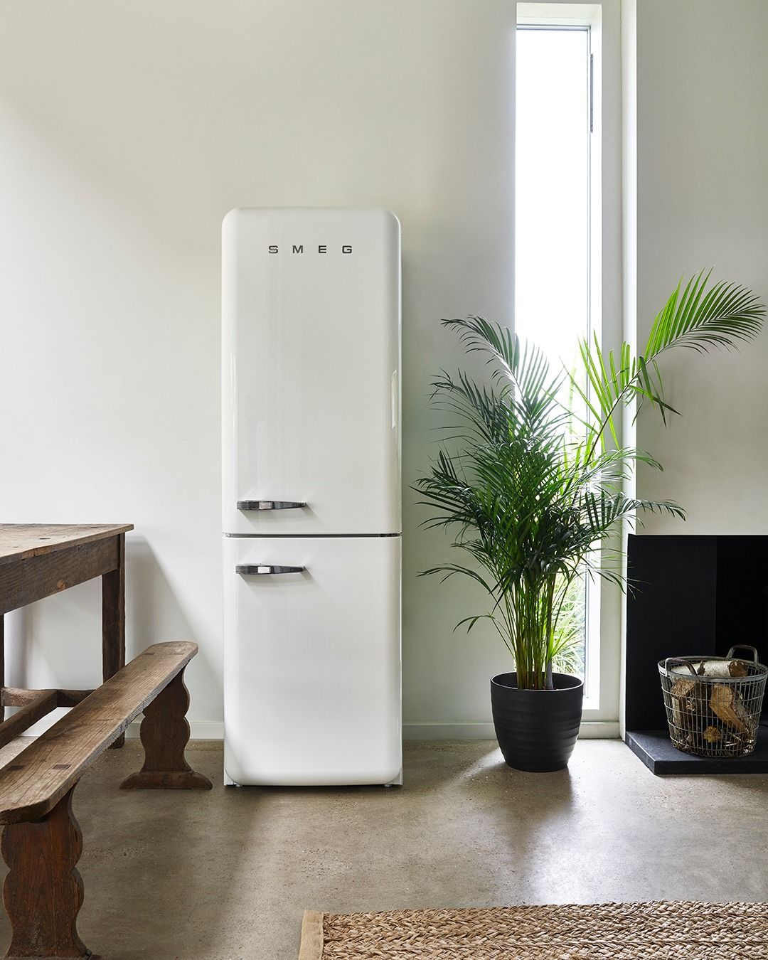 Uma geladeira branca está em uma sala de estar ao lado de um vaso de planta.