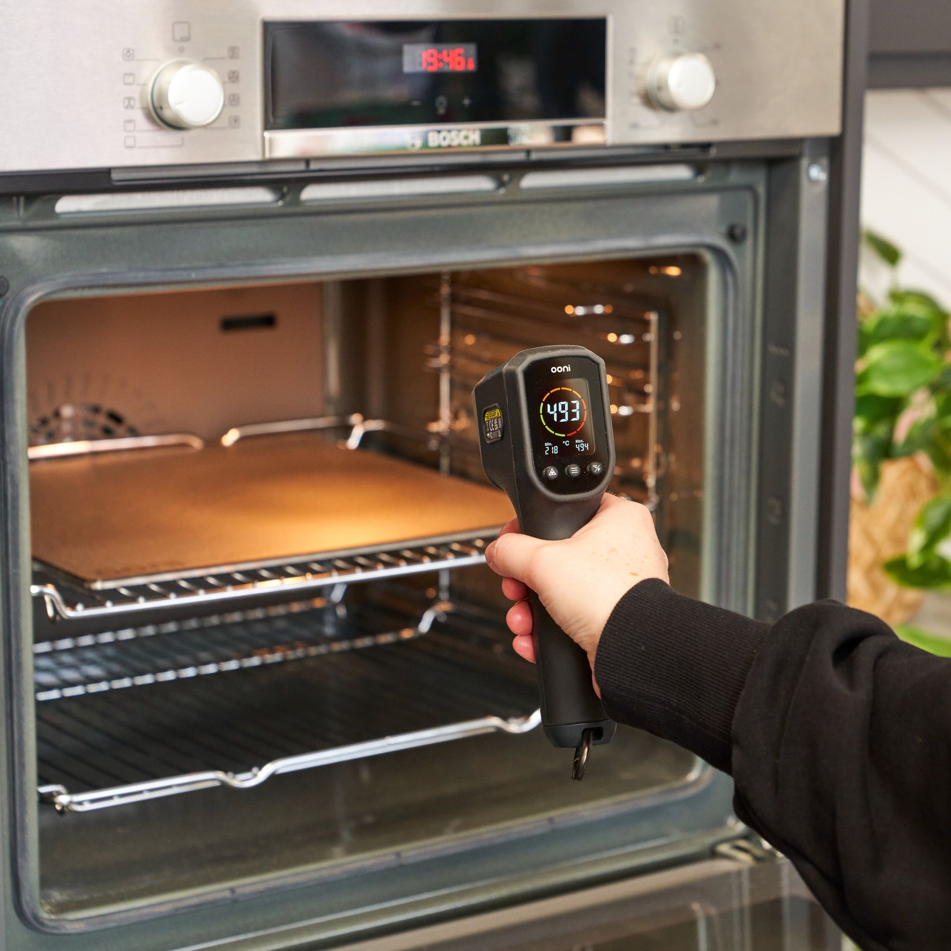 Uma pessoa está segurando um termômetro na frente de um forno Bosch