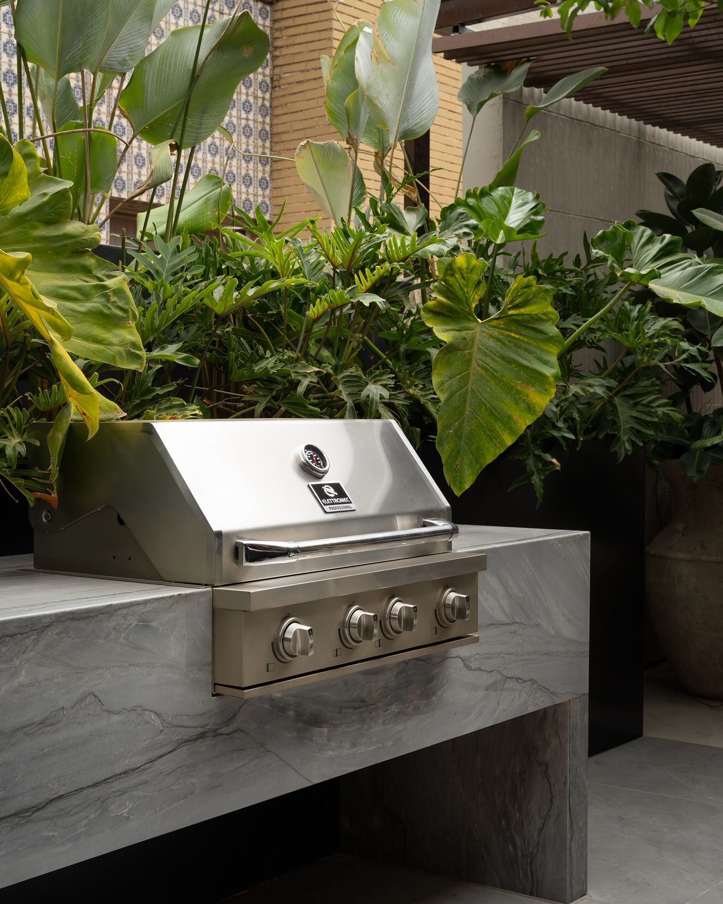 Uma grelha de aço inoxidável está em cima de um balcão de mármore cercado por plantas.