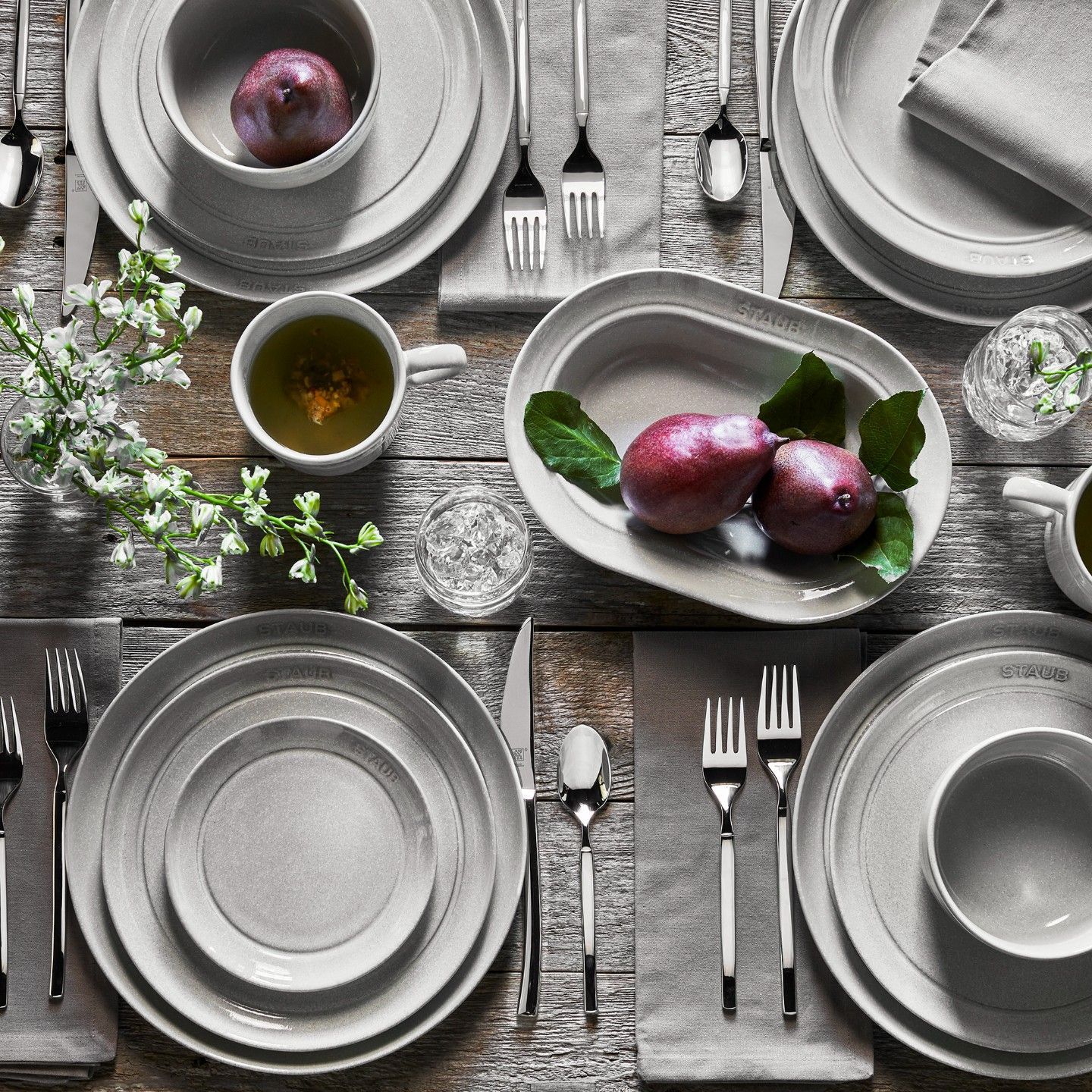 Uma mesa de madeira com pratos, tigelas, utensílios e uma fruteira.