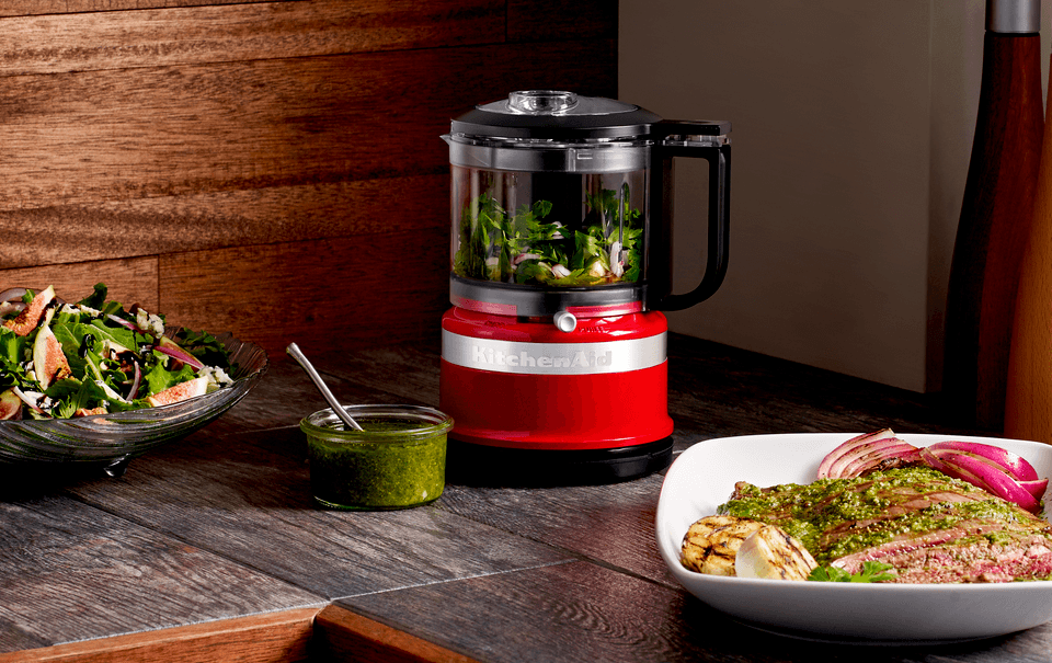 Um processador de alimentos kitchenaid está em um balcão próximo a um prato de comida.