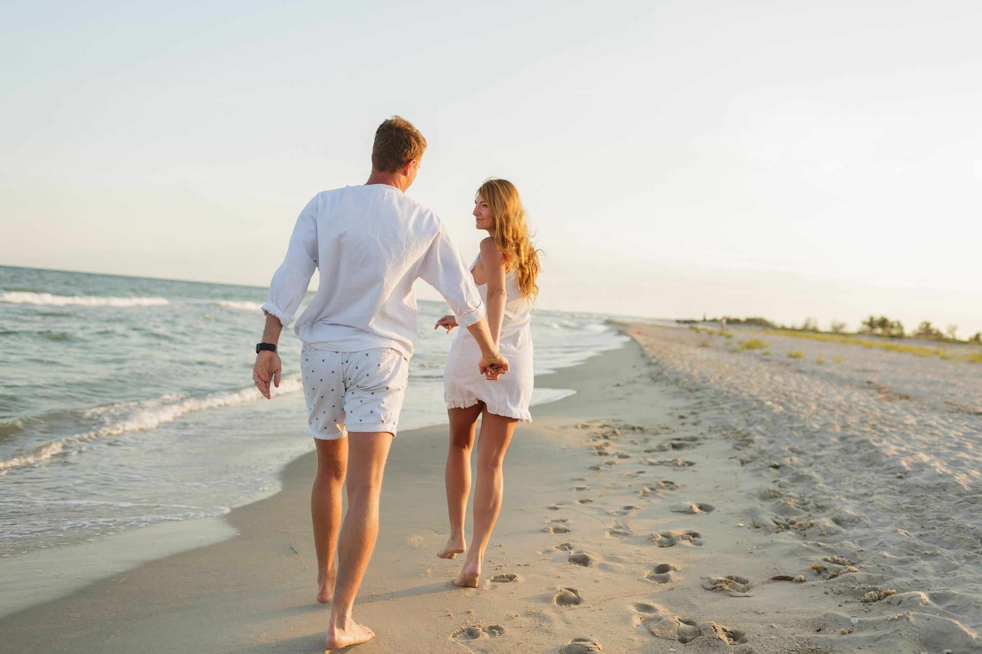 A man and a woman are walking on the beach holding hands.