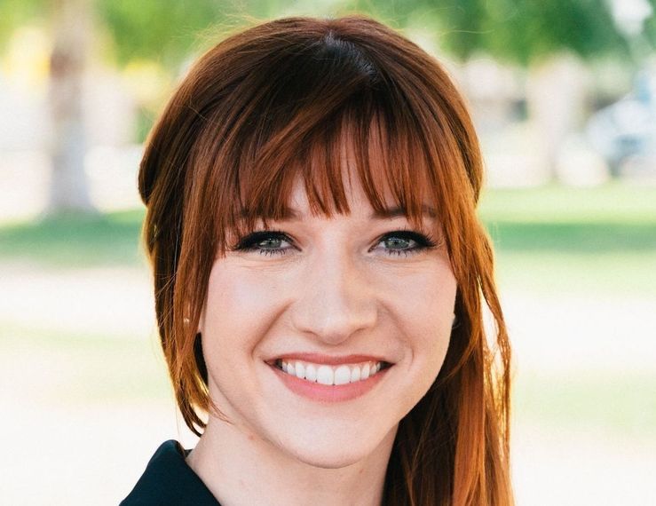 A woman with red hair and bangs is smiling for the camera.