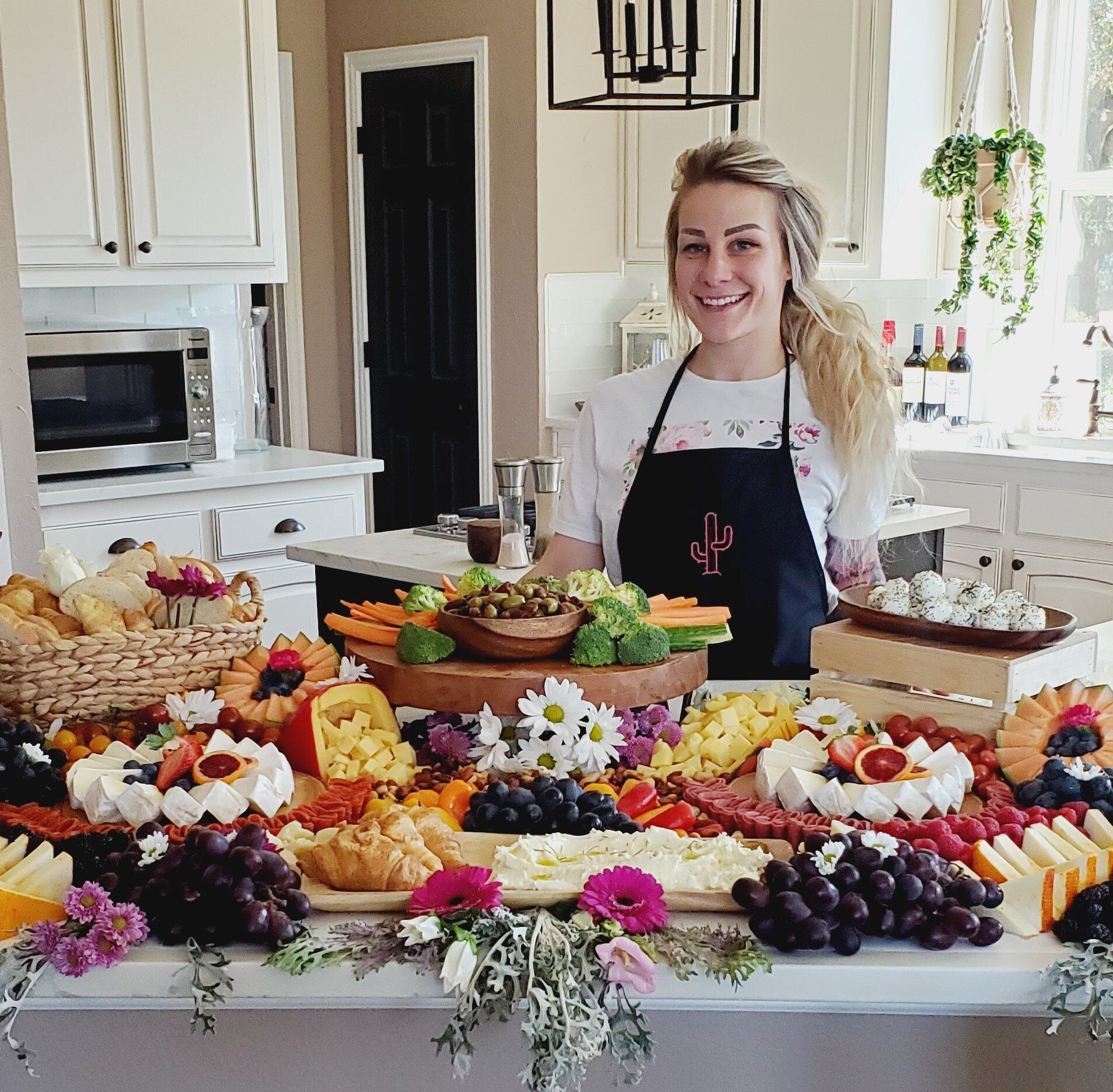 A woman in an apron is standing in front of a table full of food.