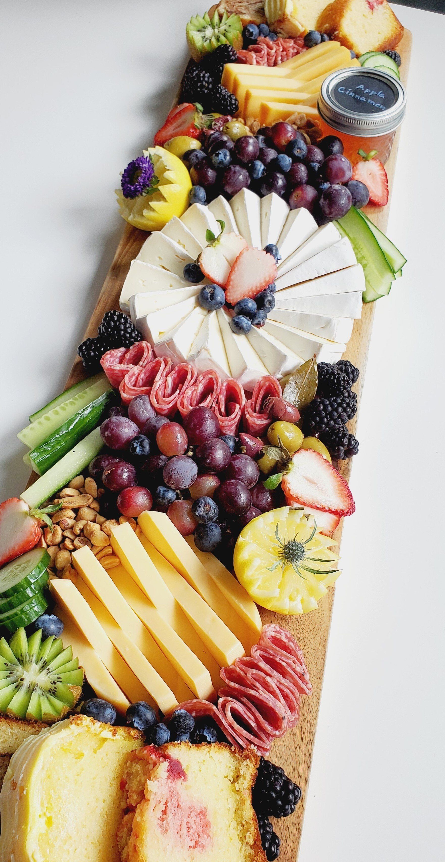 A long wooden cutting board filled with cheese , fruit , and bread.