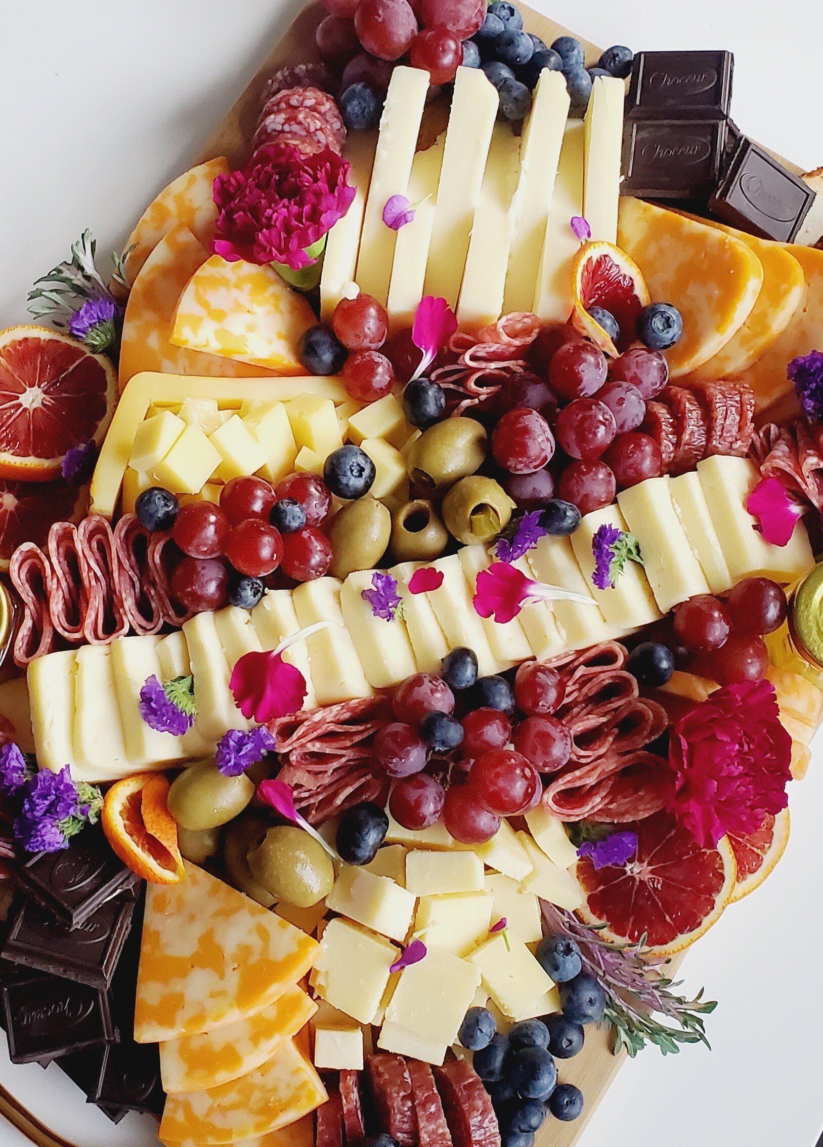A cutting board filled with cheese , grapes , olives , and other foods.