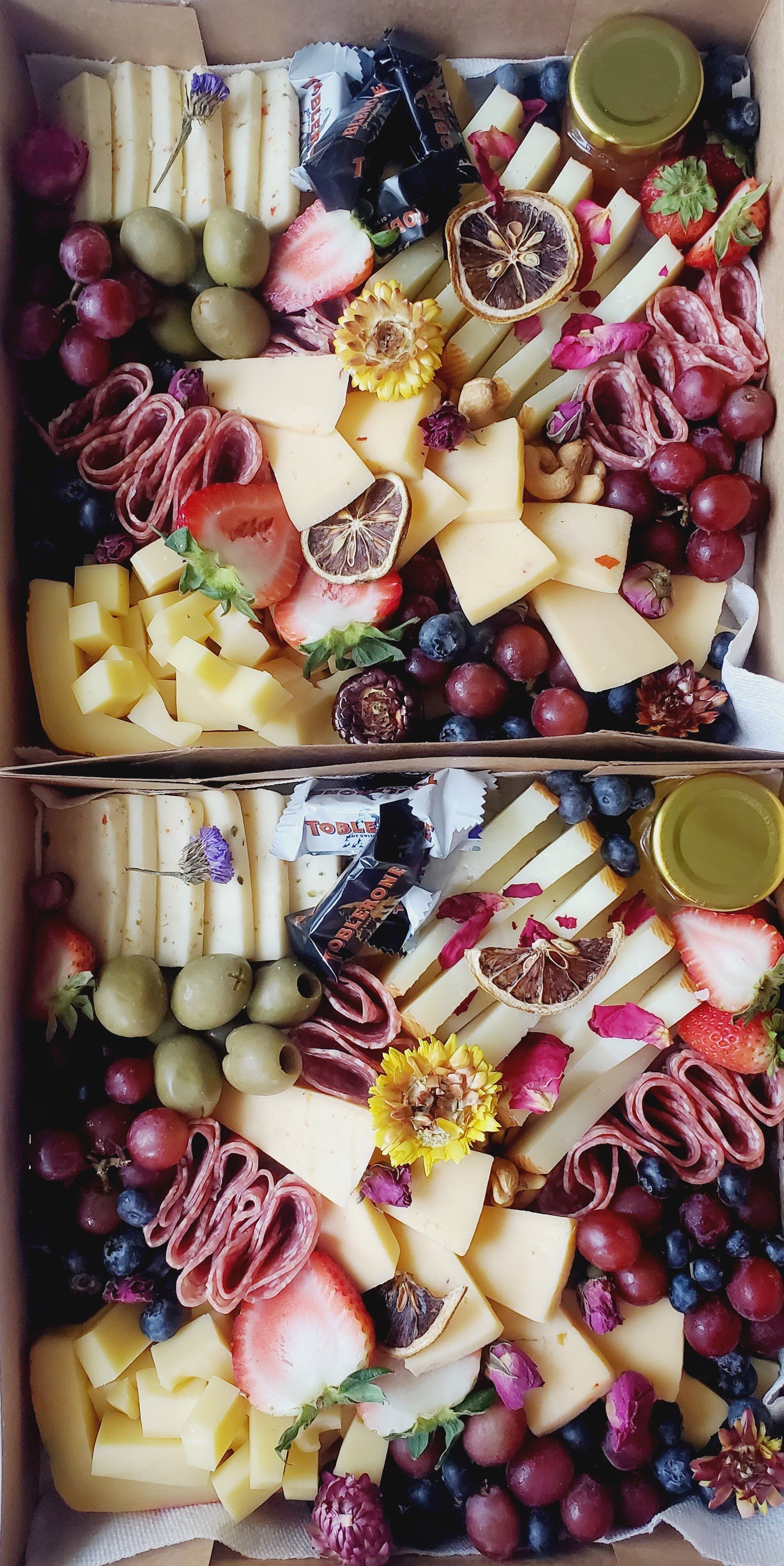 Two boxes filled with cheese , grapes , strawberries and other fruits.