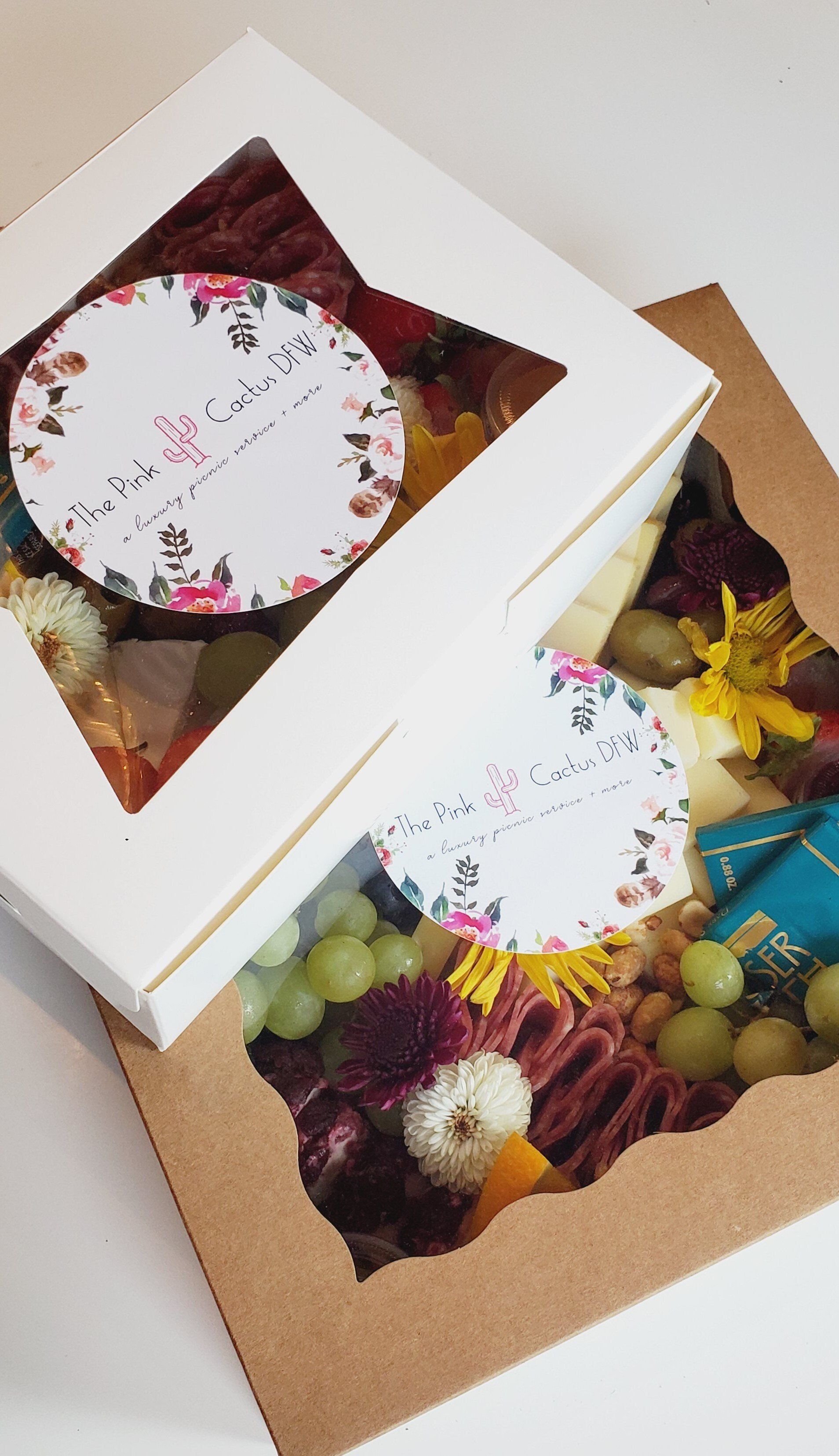 Two boxes filled with food and flowers are sitting on top of each other on a table.