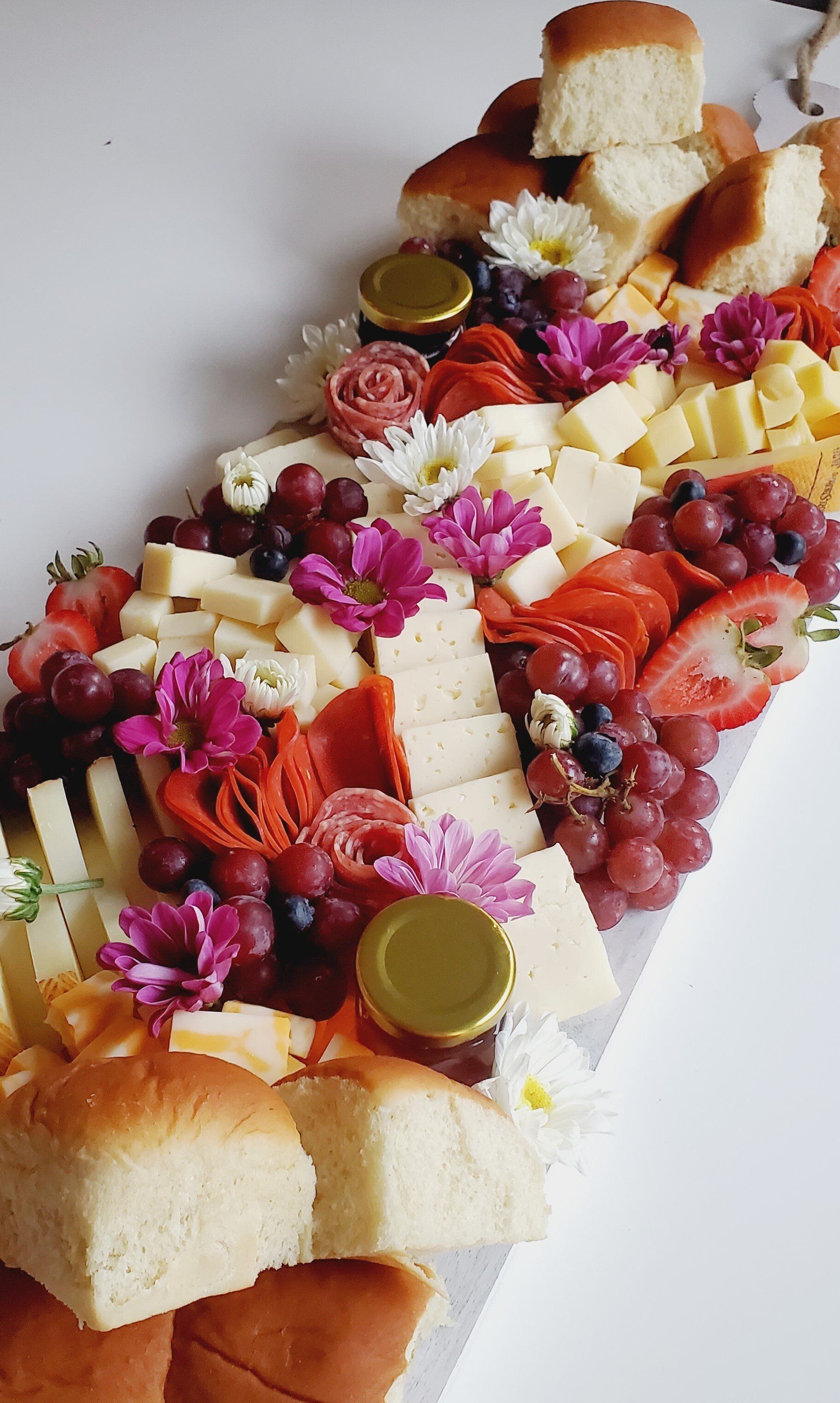 A long tray filled with bread , cheese , grapes , and flowers.