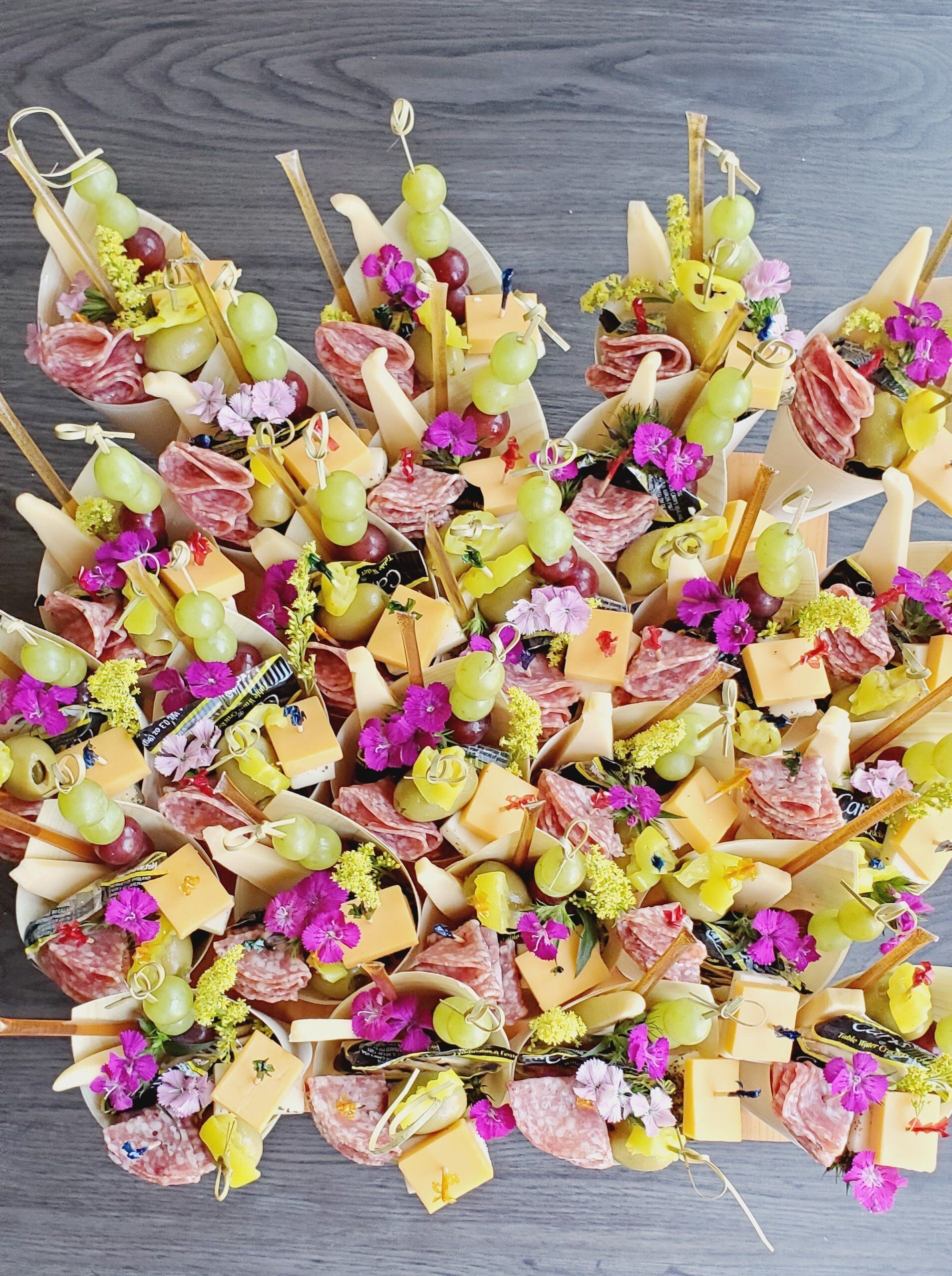 A tray of food with meat , cheese , grapes and flowers on a table.