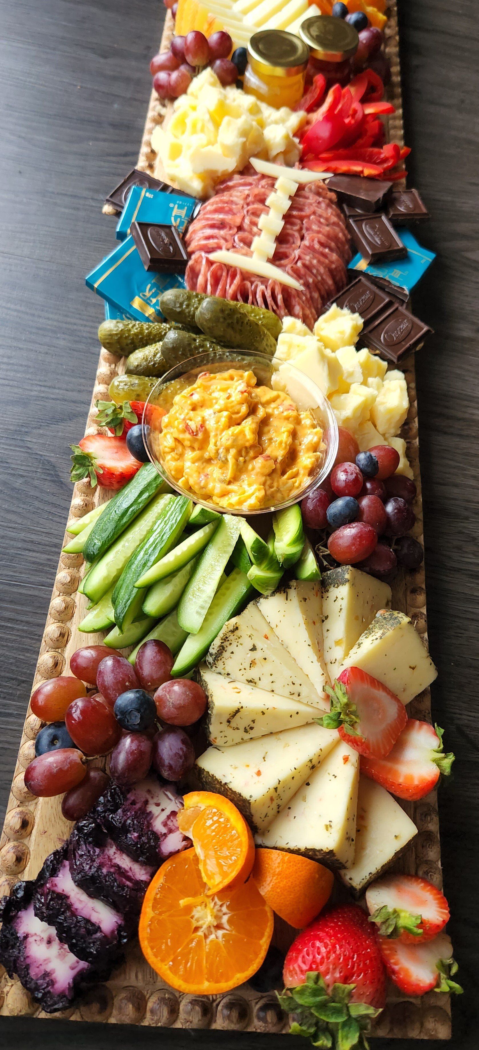 A long cutting board filled with cheese , fruit , vegetables and meat.
