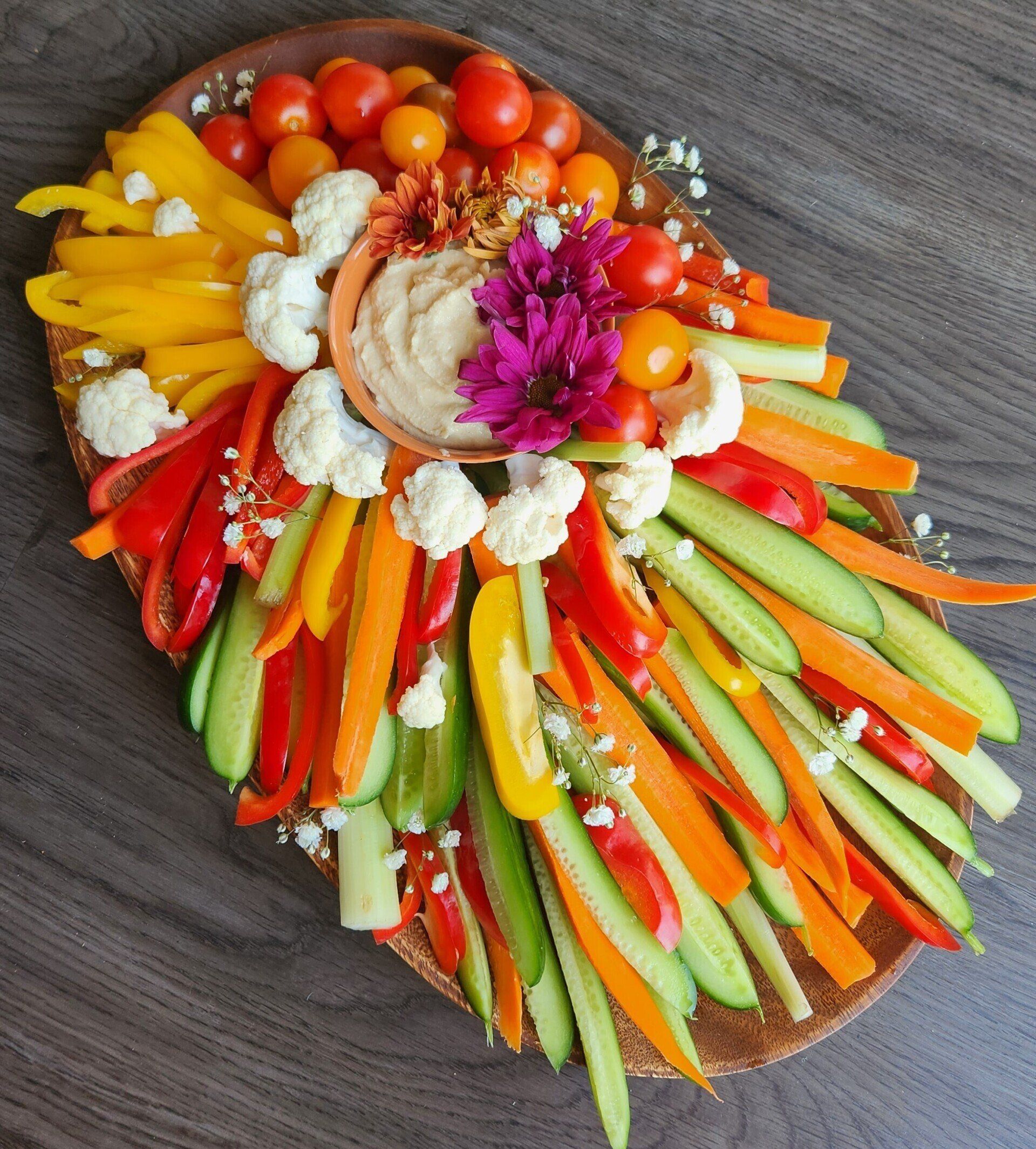 A wooden cutting board filled with vegetables and dip on a table.