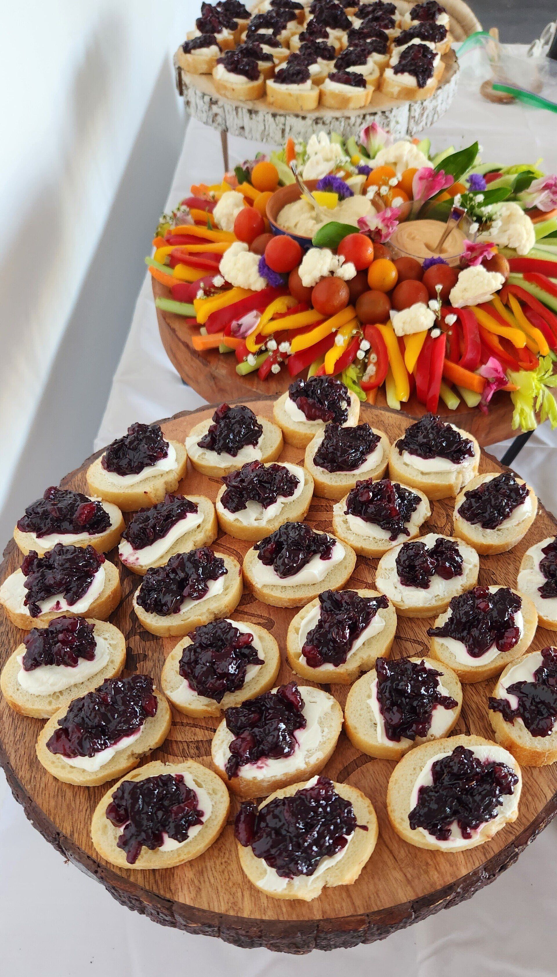 A wooden cutting board topped with appetizers and vegetables on a table.