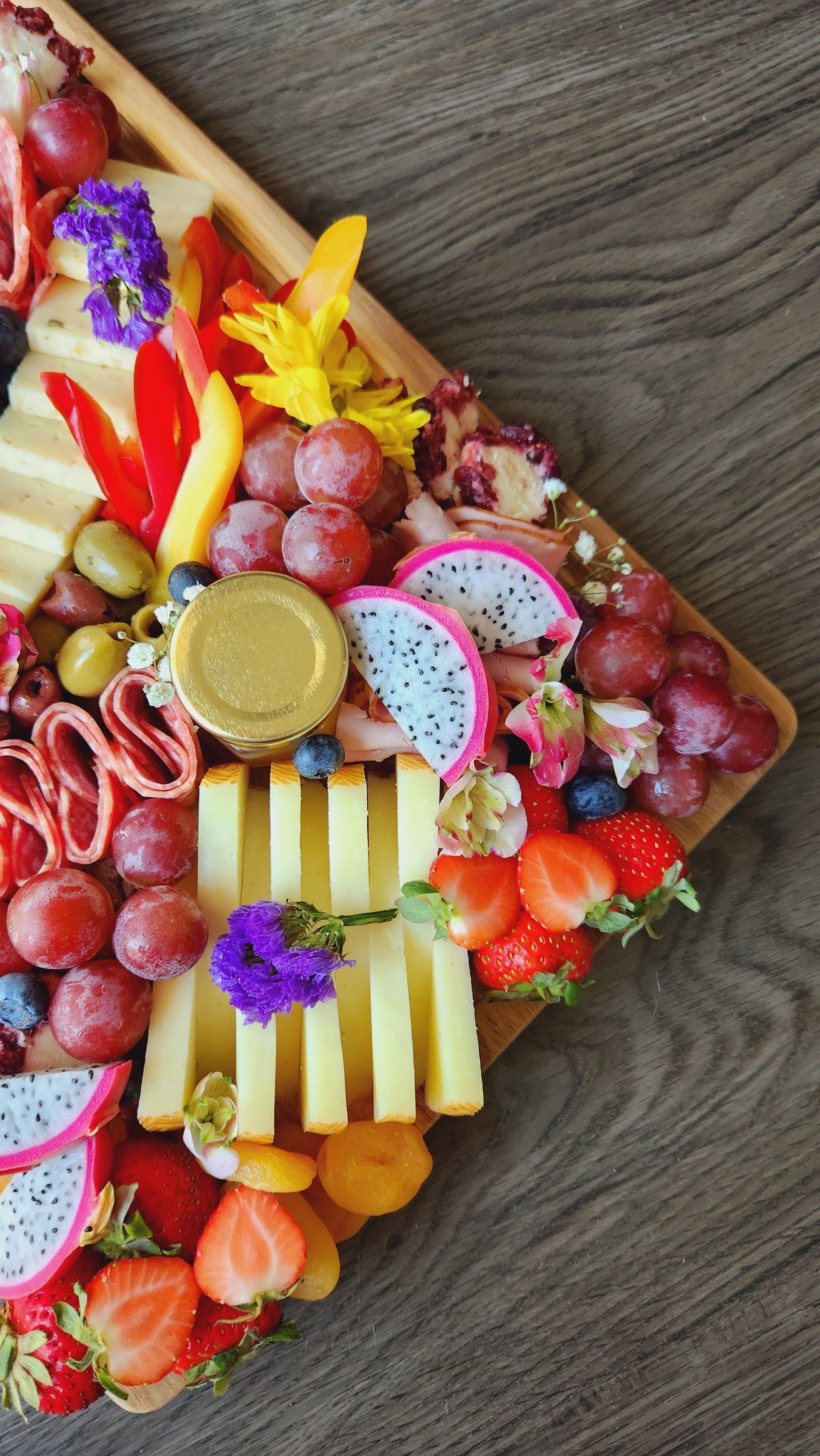 A wooden cutting board filled with fruit and cheese on a wooden table.