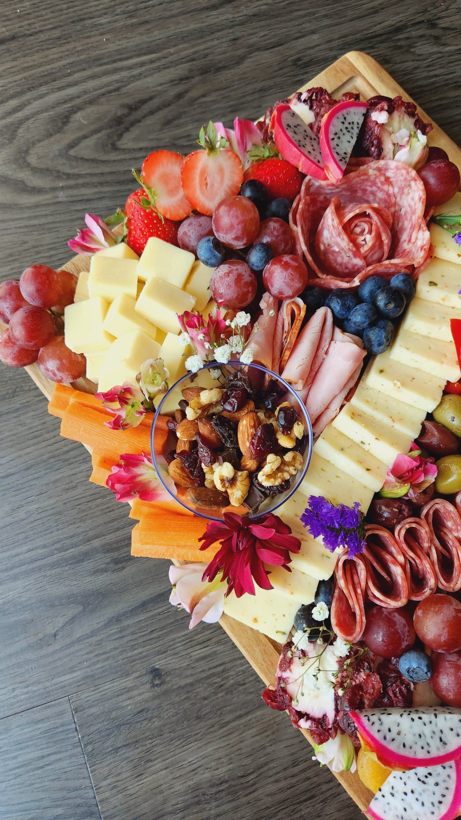 A cutting board filled with cheese , fruit , meat and nuts on a wooden table.