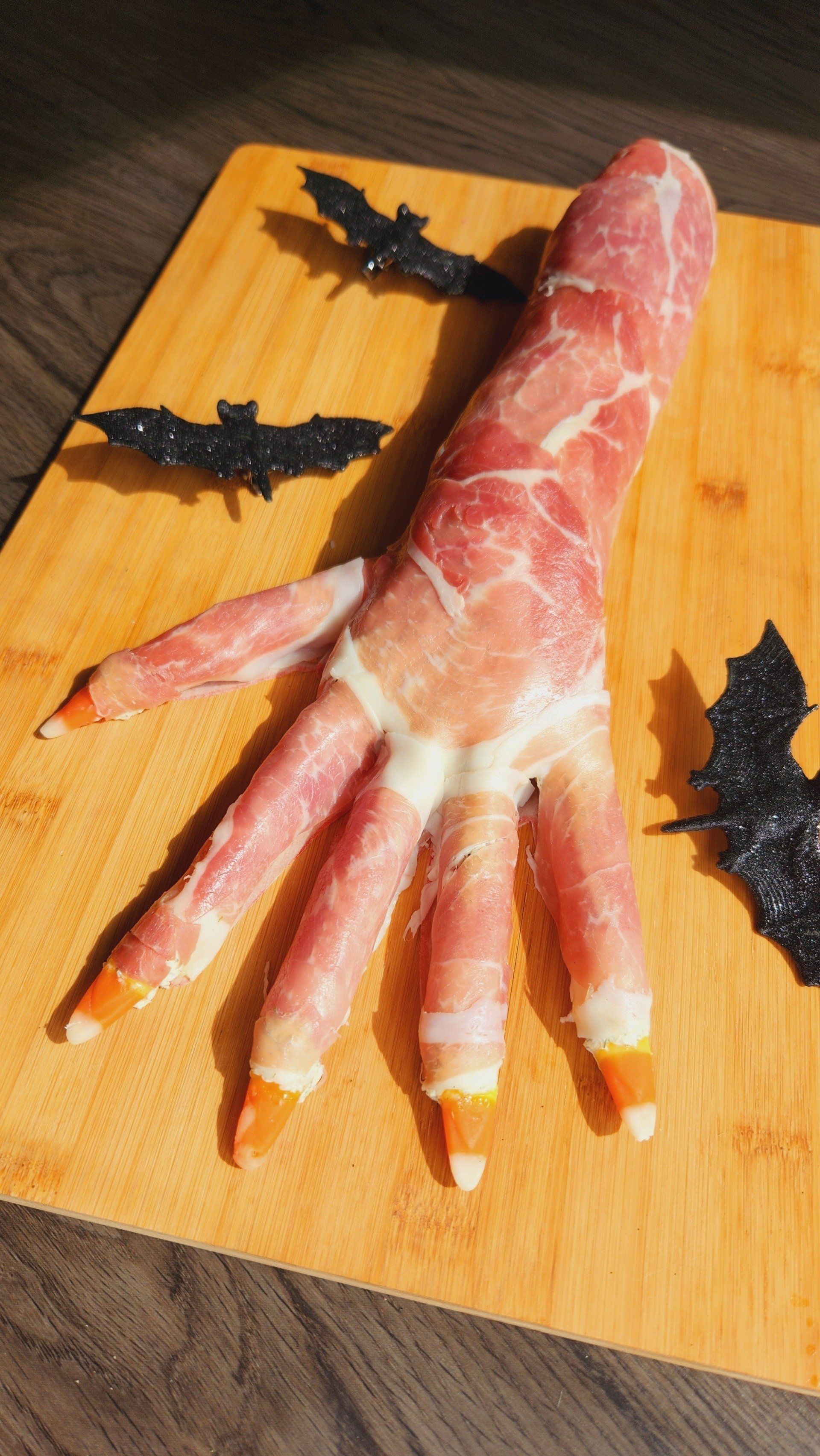 A hand made out of bacon and candy corn on a cutting board.