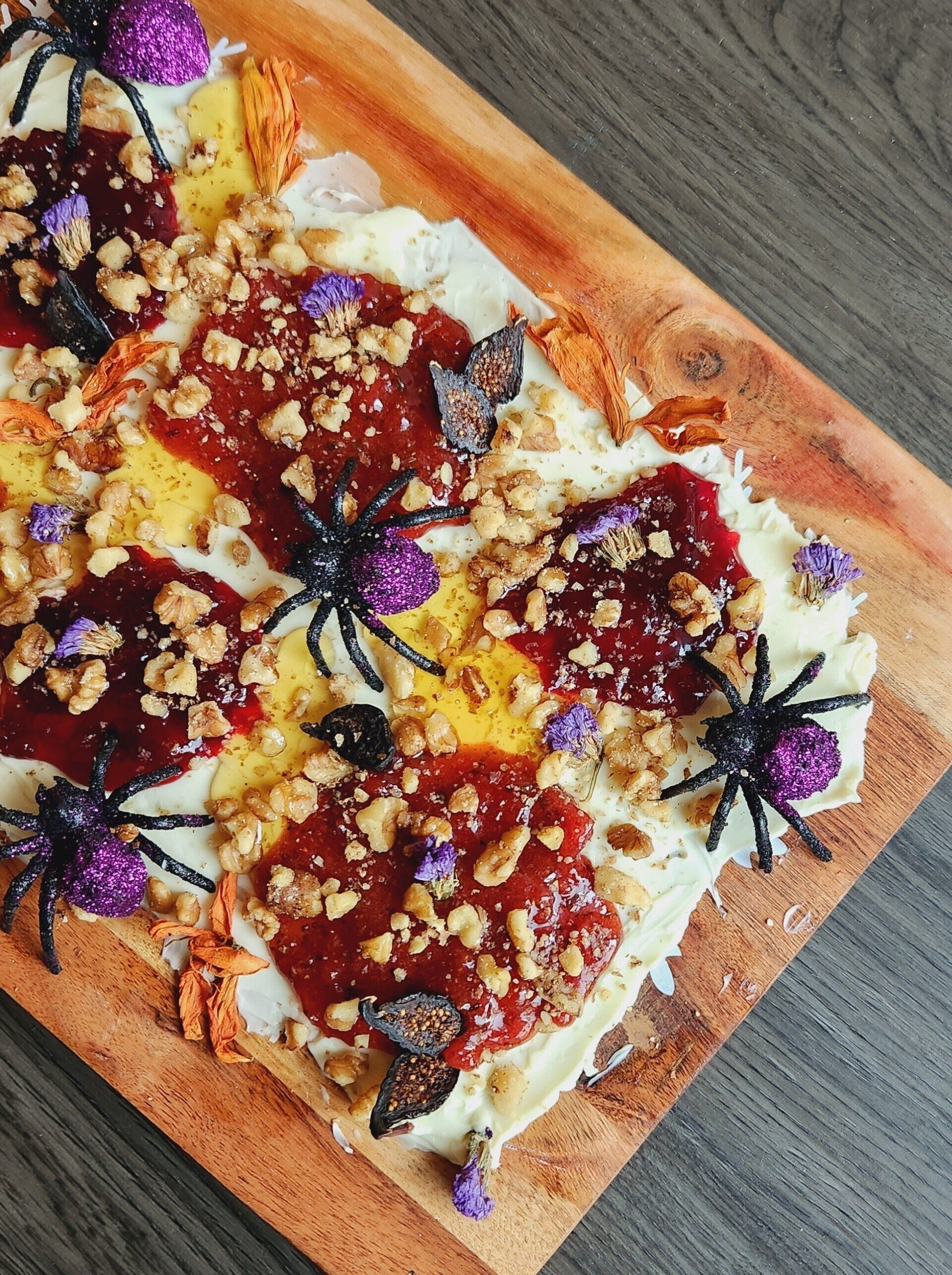 A pizza with spiders and nuts on it is on a wooden cutting board.