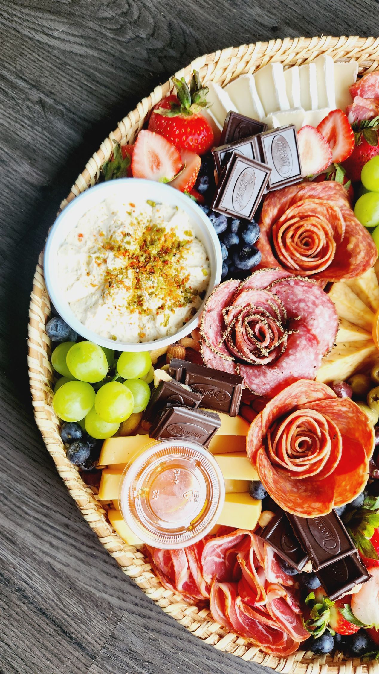 A heart shaped tray filled with meat , cheese , berries and chocolate.