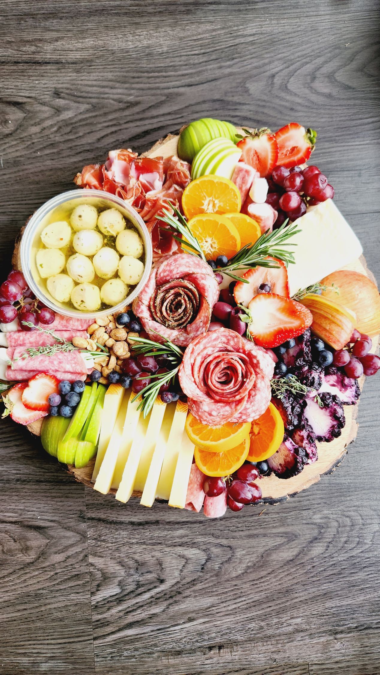 A wooden cutting board topped with meat , cheese , fruit and nuts.