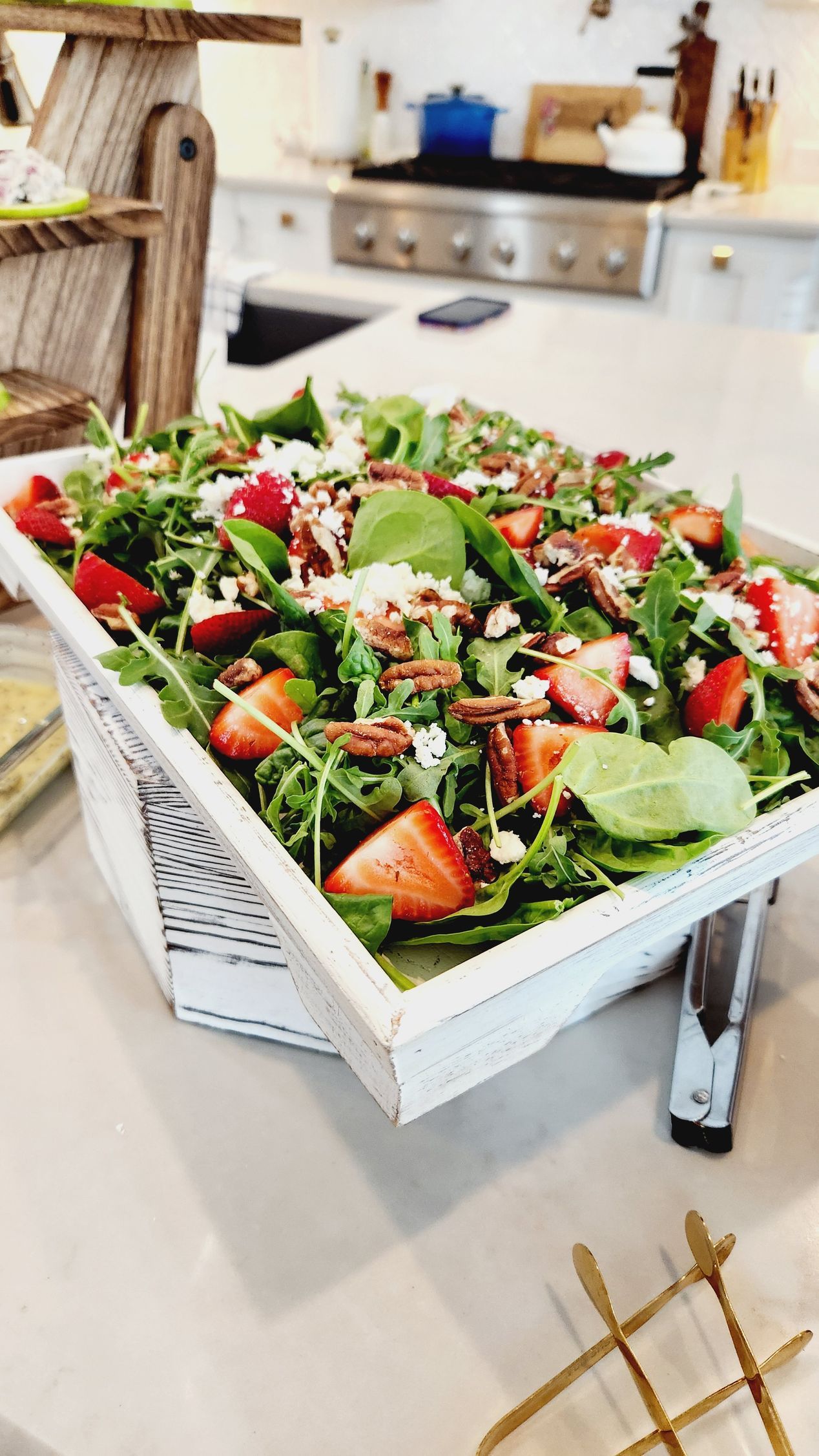 A salad with strawberries and pecans is sitting on a white tray on a table.