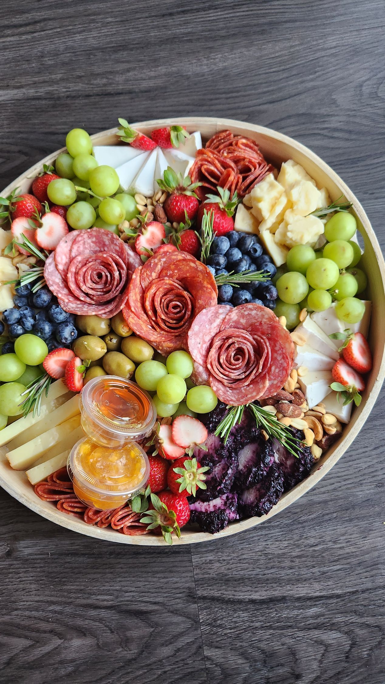 A plate of food with grapes , strawberries , blueberries , olives , and meat on a wooden table.